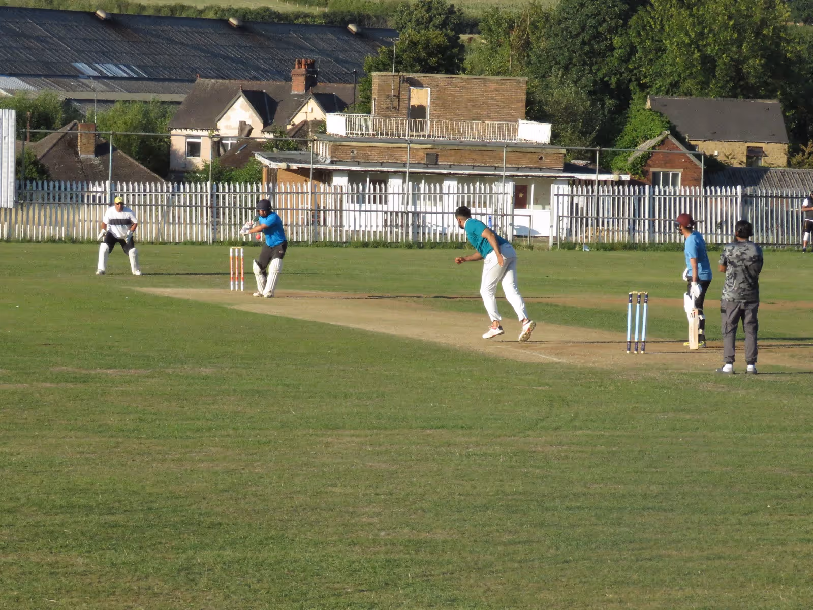 Action shot of Haroon making room to play an offside shot at Caribbean Sports Club, with the keeper, umpire, and both YCF and Cricket Arena stumps visible in a picturesque setting.