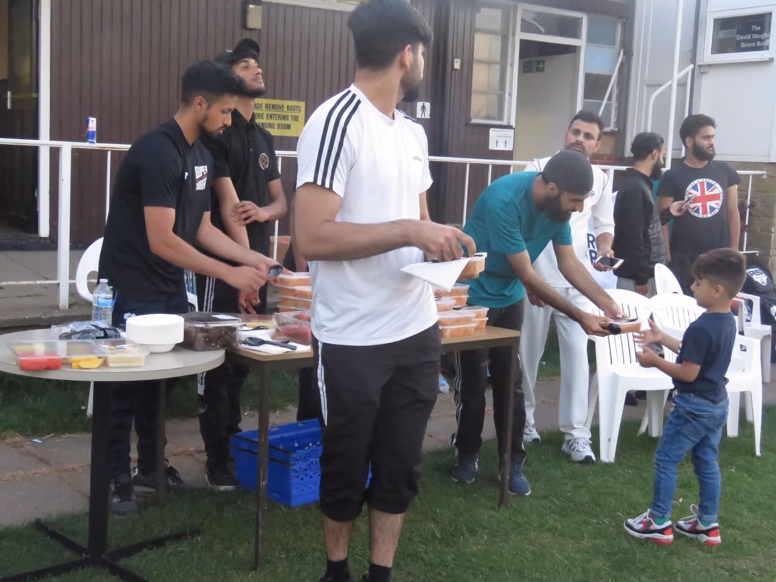 “Volunteers at Caribbean Sports Club serve food after the final, as one volunteer hands a meal to a young child — capturing intergenerational connection and community spirit.”