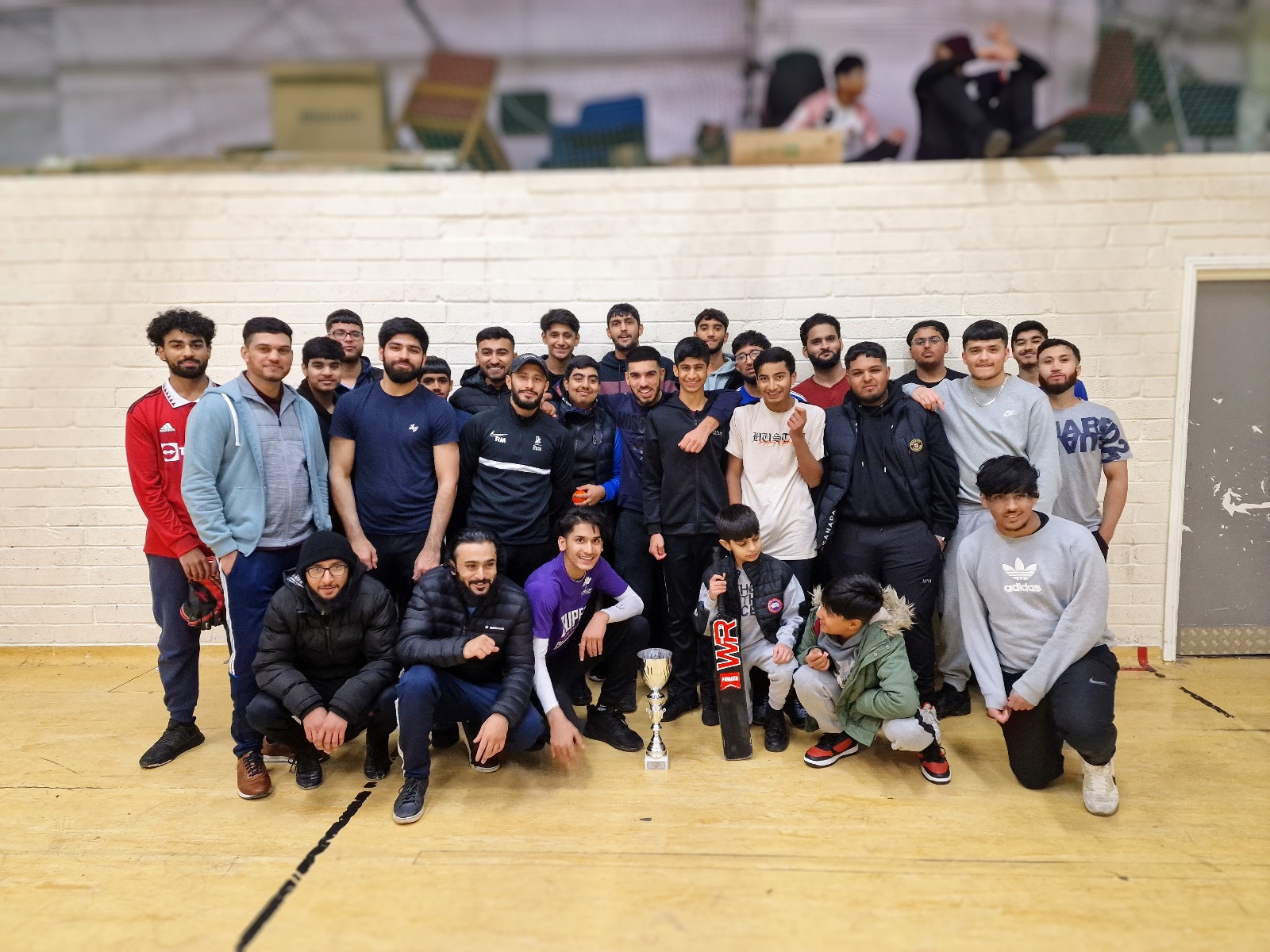 Large group of league players smiling together after finals at YMA Sheffield holding bats and trophies celebrating unity
