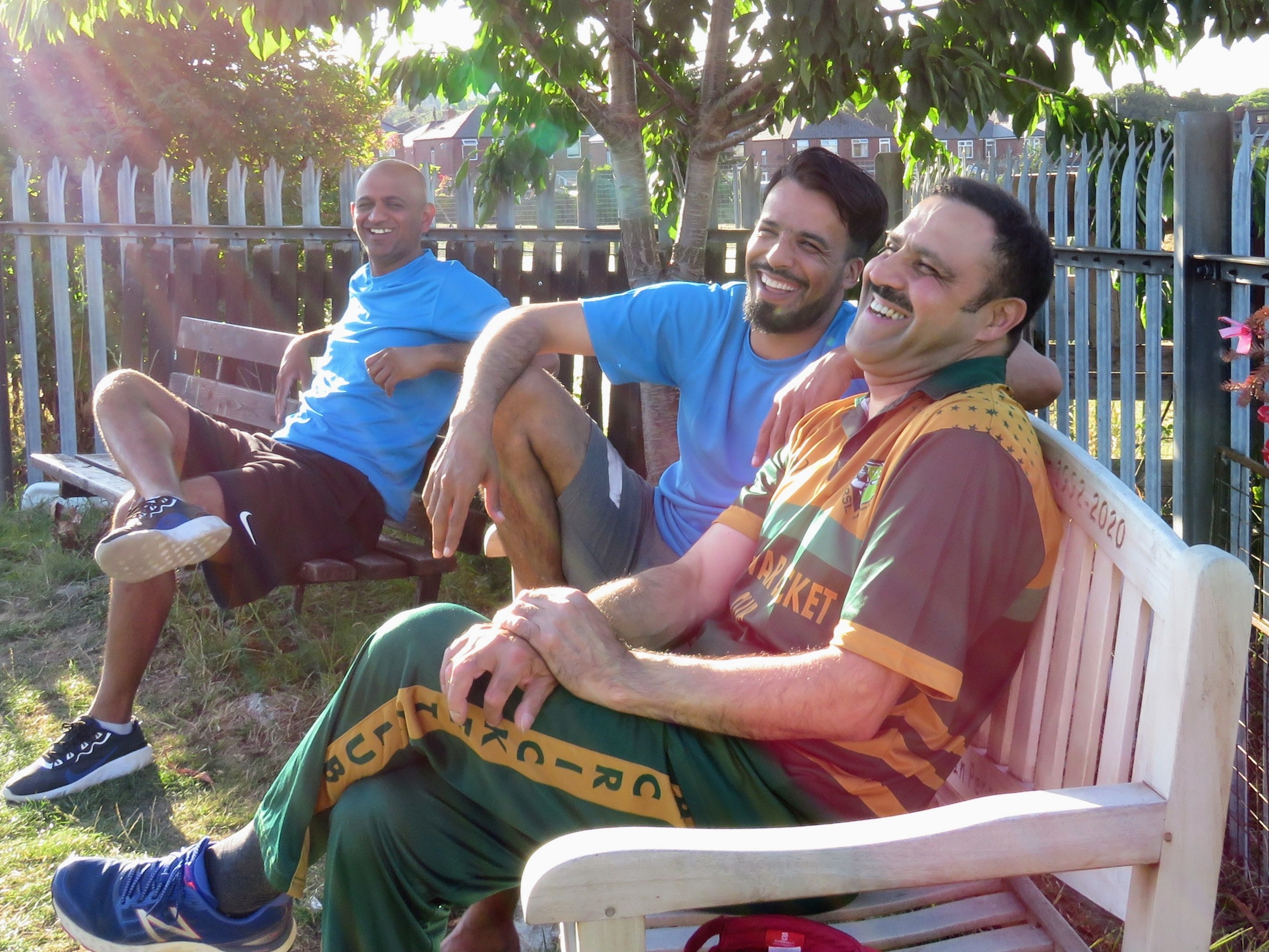 Cricket Arena players from different generations share laughter on benches during outdoor cricket session in Sheffield