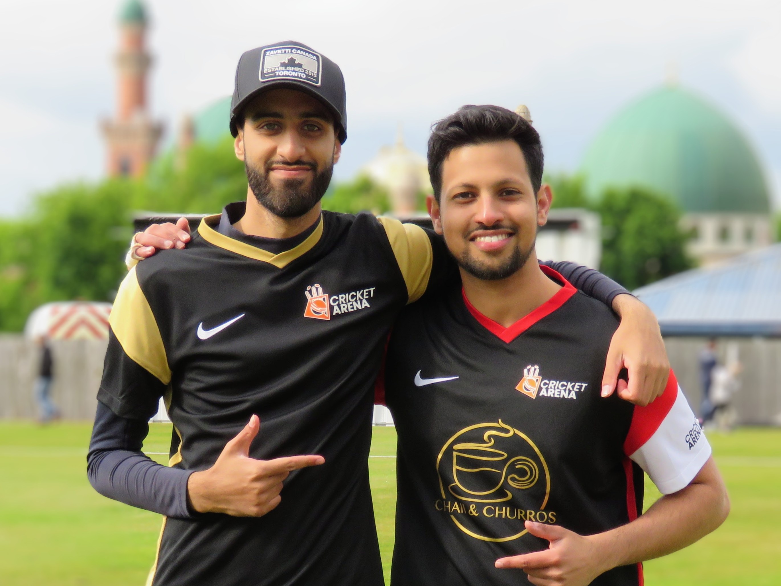 Two Cricket Arena volunteers and league managers pose in club kit, highlighting the volunteer leadership behind events