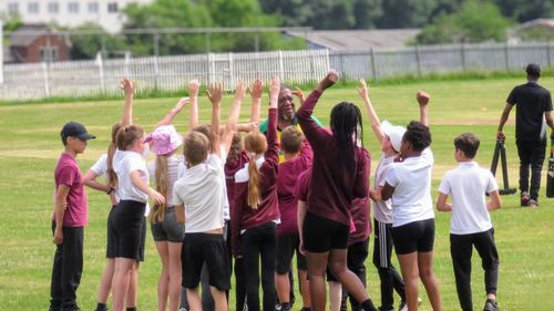 School children cheer with their hands raised as coach Milton Samuels energises the group during the Windrush75 cricket session at Sheffield Caribbean Sports Club.