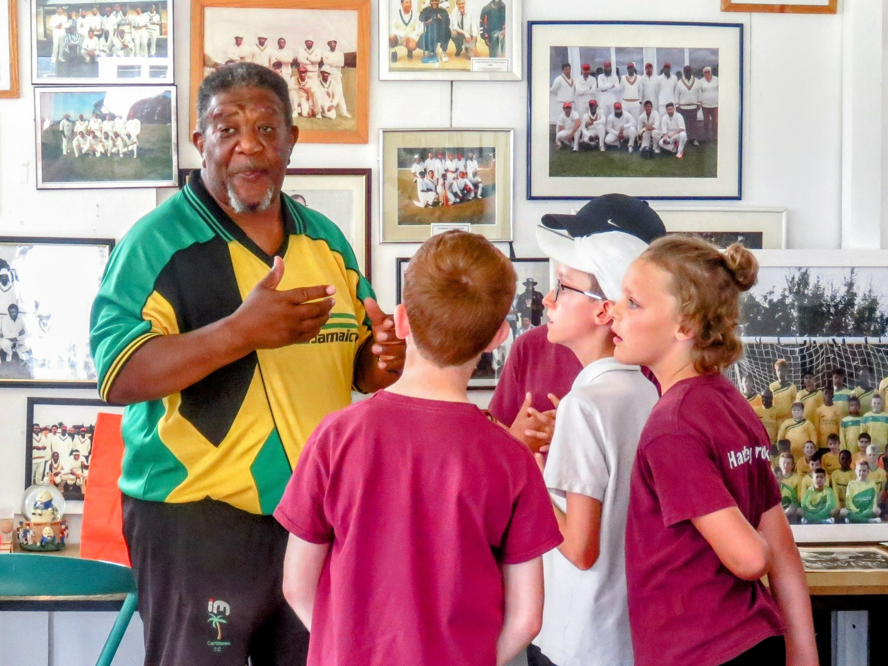 Milton Samuels passionately sharing Windrush stories with school children inside the Caribbean Sports Club, surrounded by historic cricket photos celebrating Caribbean heritage.