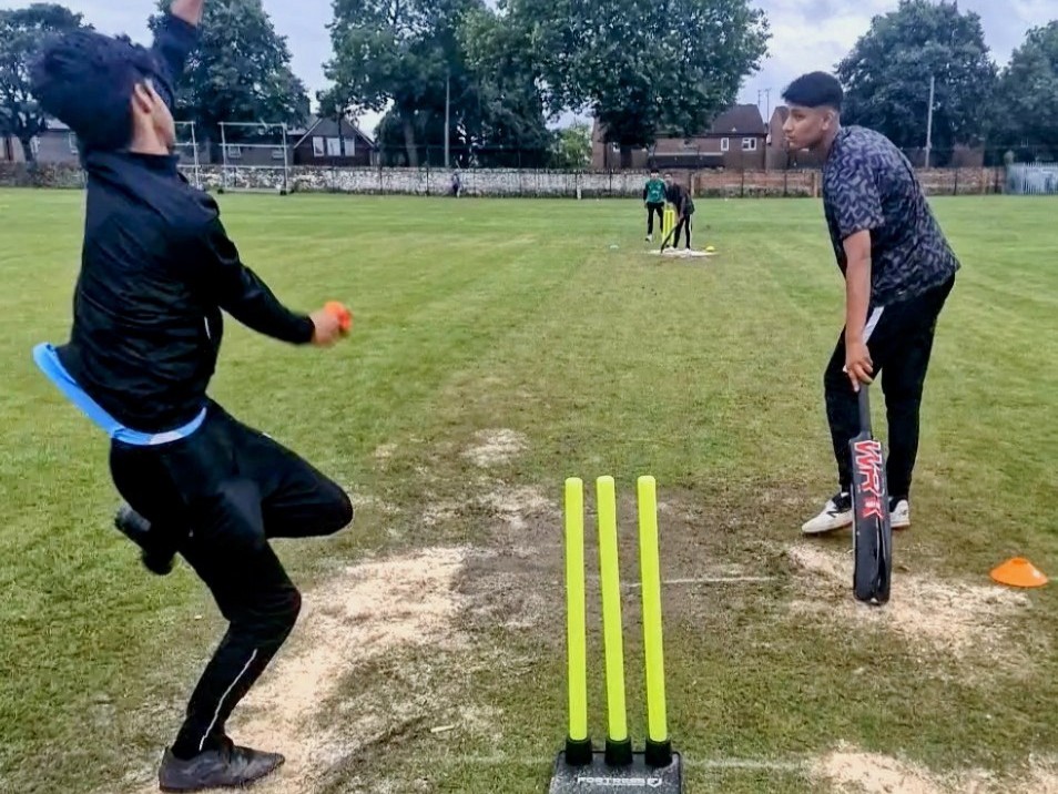 Bowler about to bowl as the batter watches closely at Shiregreen Cricket Club during the Junior Hundred. The grass wicket is patched with sand after rain on a wet, cloudy day.