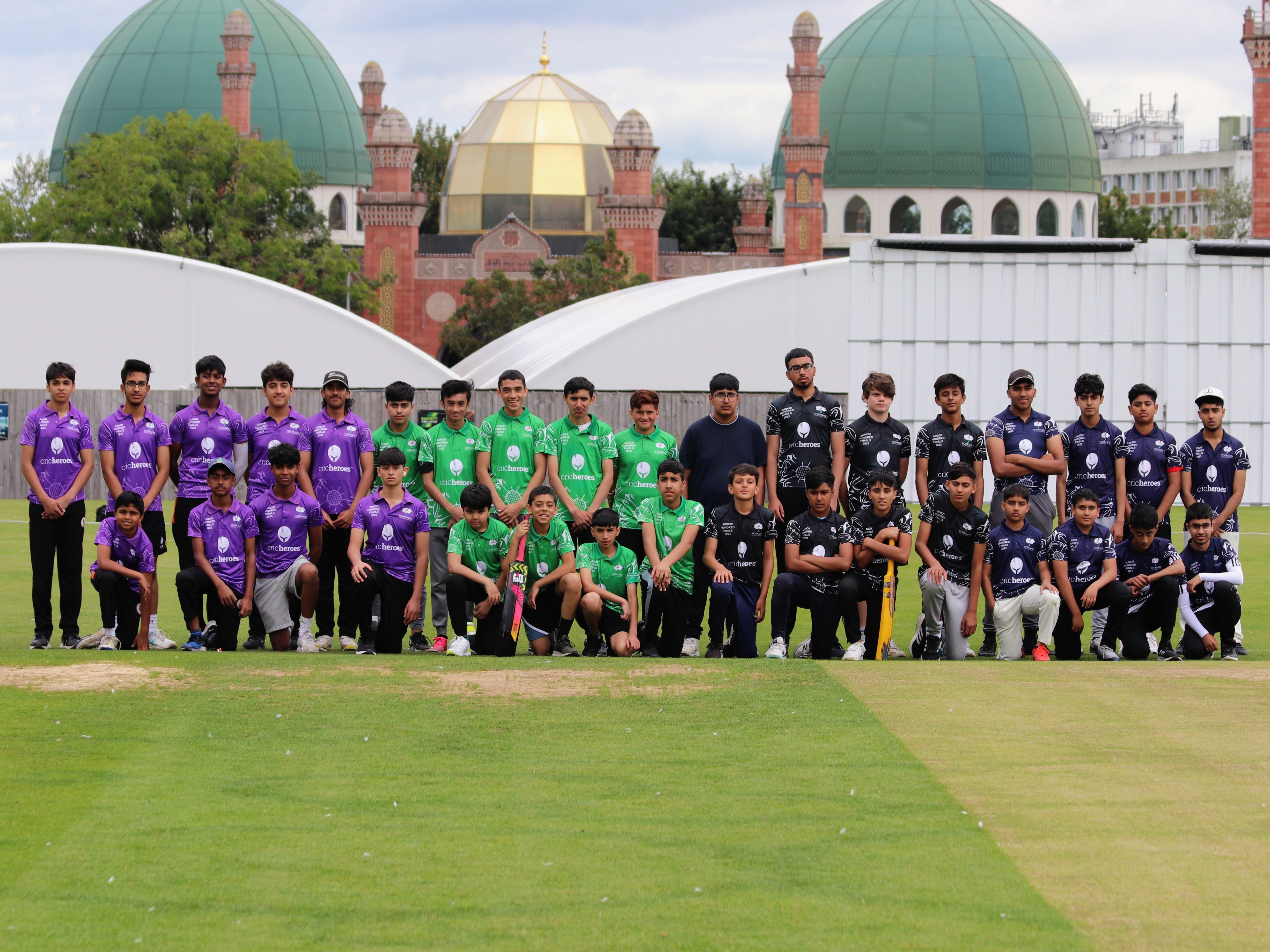 All four teams from the Yorkshire Junior Hundred 2023 pose together at Park Avenue, Bradford, with the mosque domes in the background — players in purple, green, and black kits representing different regions including Sheffield.