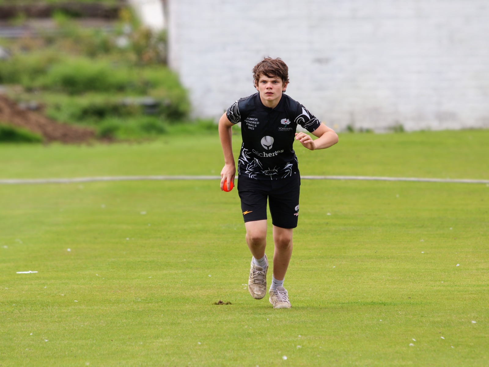 A Sheffield player in the Yorkshire black kit runs in to bowl during the Yorkshire Junior Hundred 2023 match at Park Avenue, Bradford.