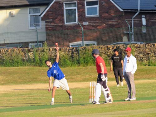 Daniyal bowls in shorts on a sunny day as umpire Sam Gitten watches, showing the relaxed and fun spirit of the league.