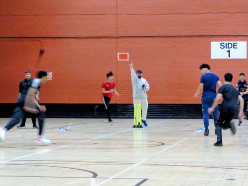 Umpire signals a wicket as fielders celebrate during MBL 2023 at Concord Sports Centre, capturing youth indoor cricket energy.