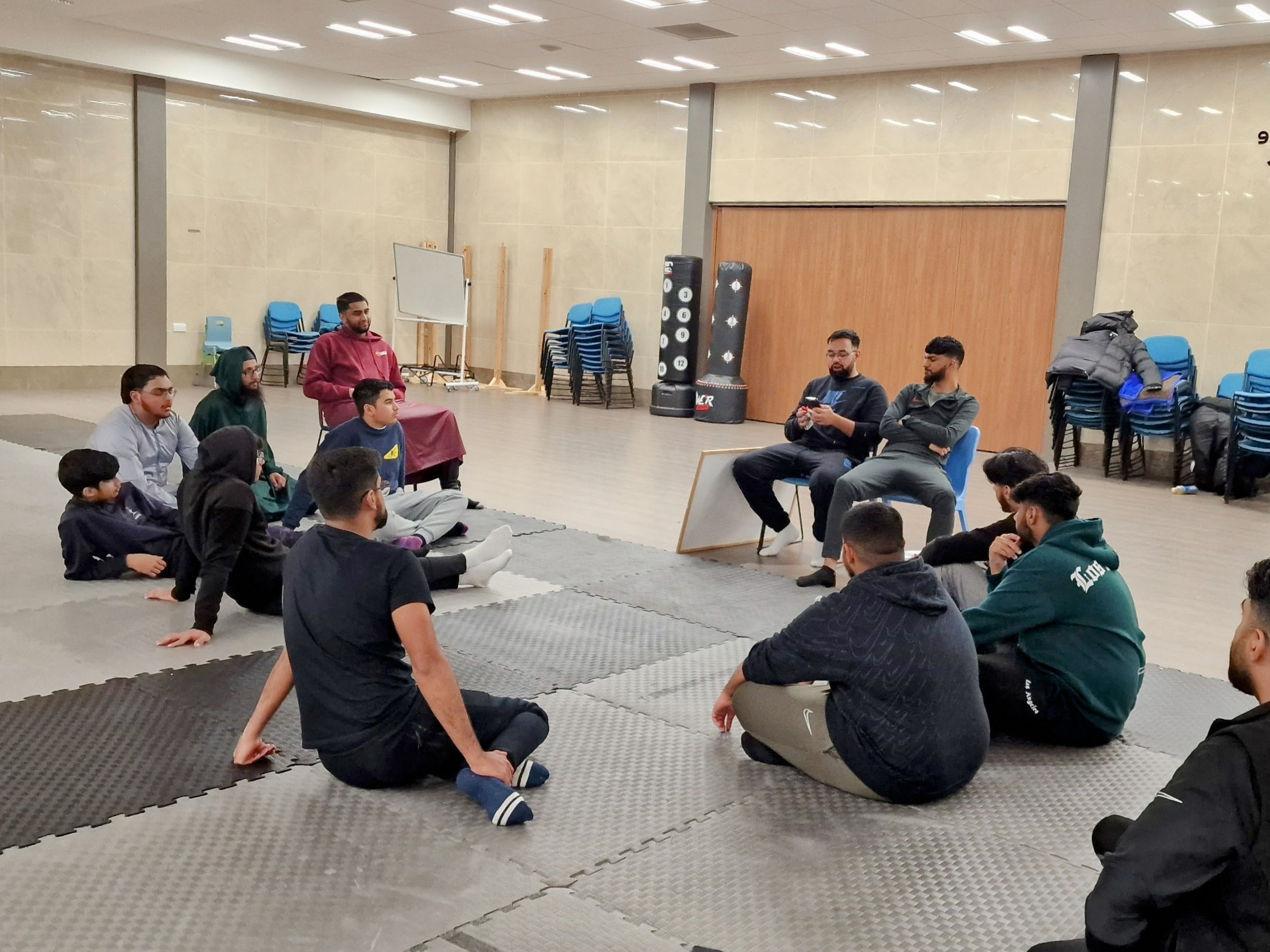 Boys aged 13–17 sit in a circle for a team talk at Sheffield Grand Mosque activity hall.