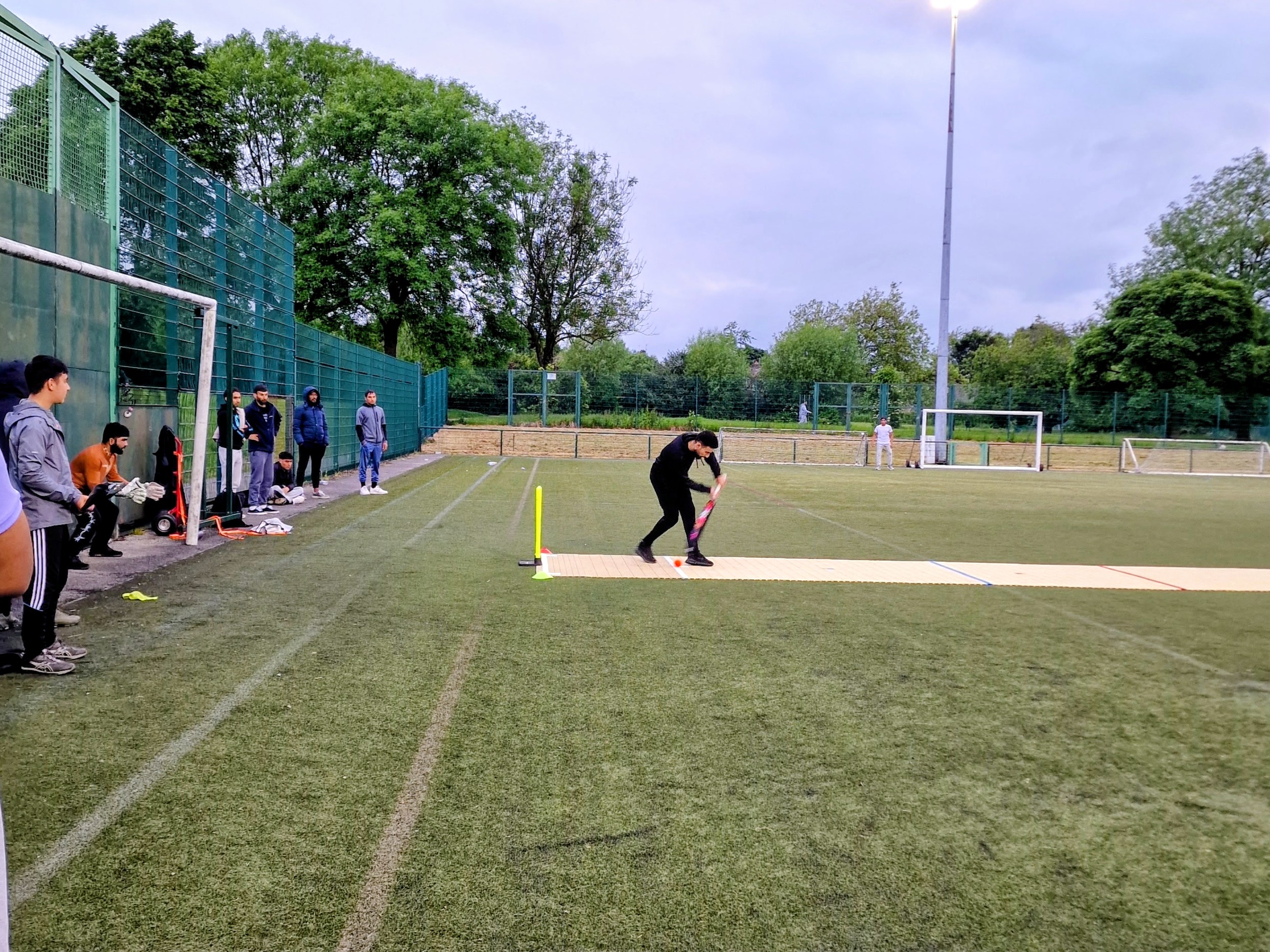 Batter plays a shot on the 2G Flicx at Concord under floodlights, teammates watching — community cricket in Sheffield.