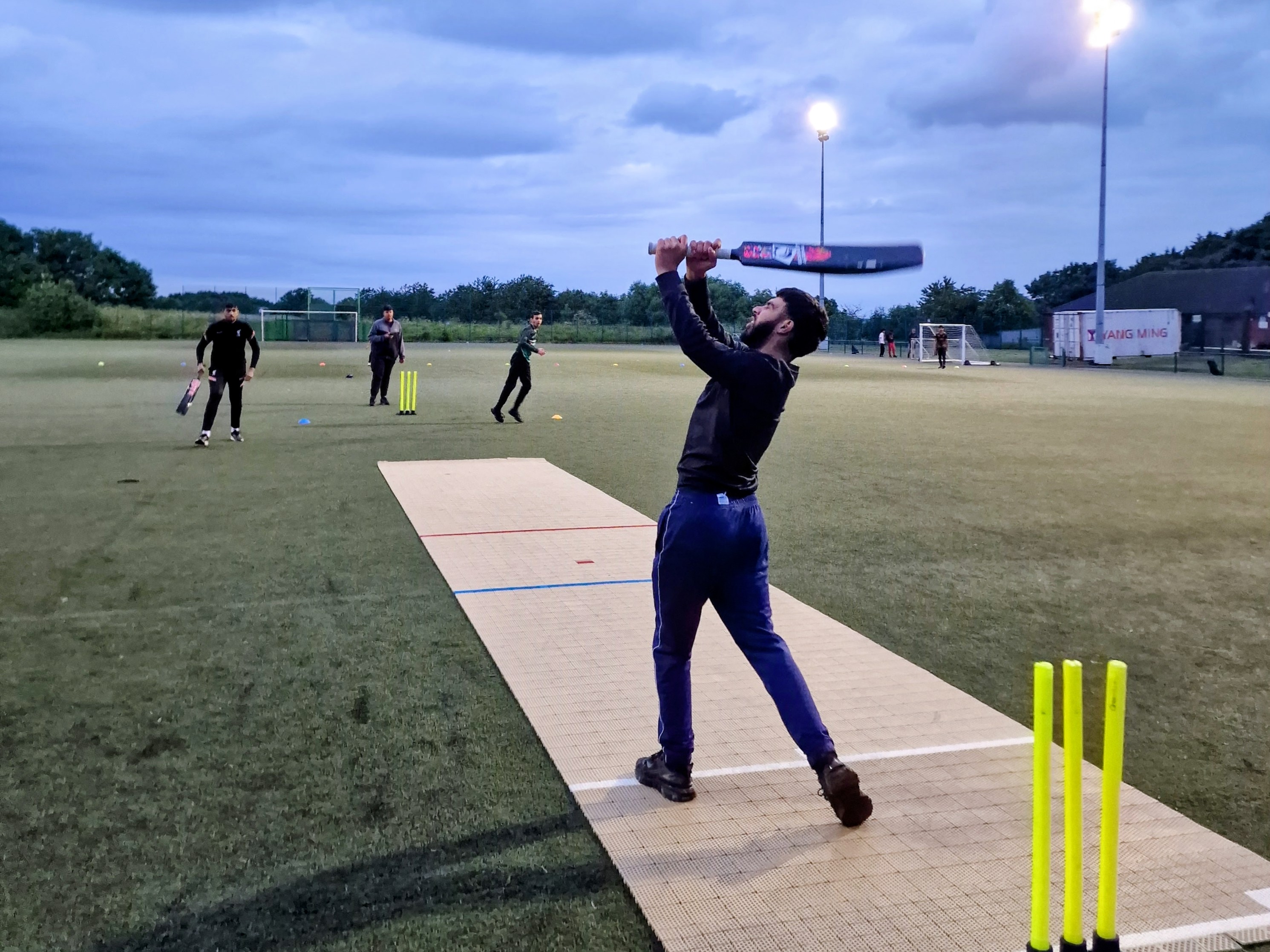 Lofted shot on the 2G Flicx pitch under evening lights at Concord — open, welcoming community cricket.