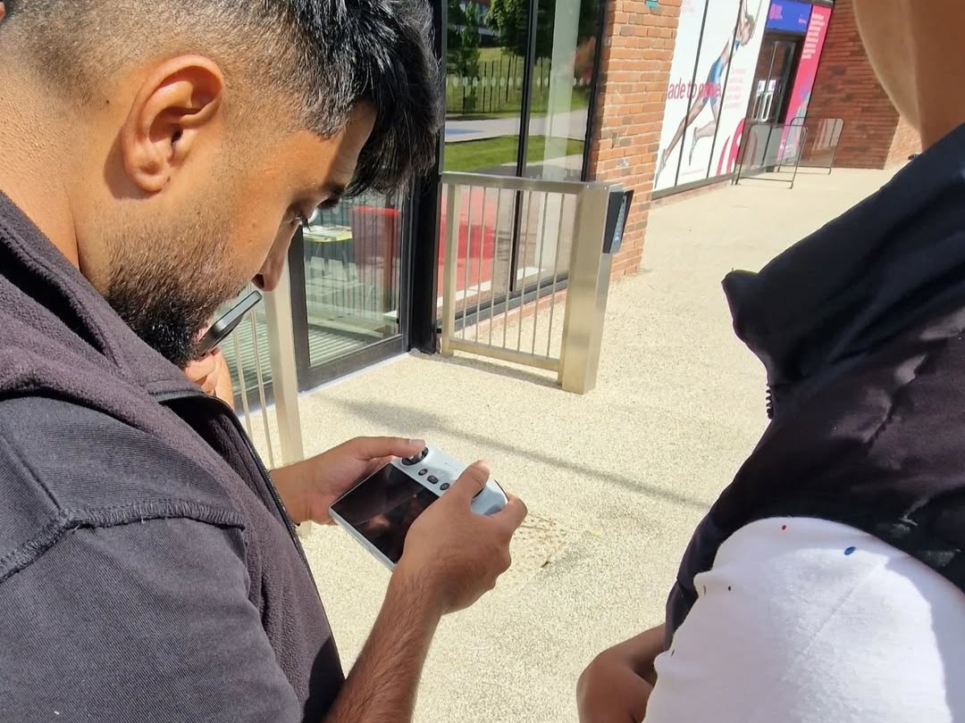 A Cricket Arena mentor demonstrates the drone controller to Zayn during media training outside the office.
