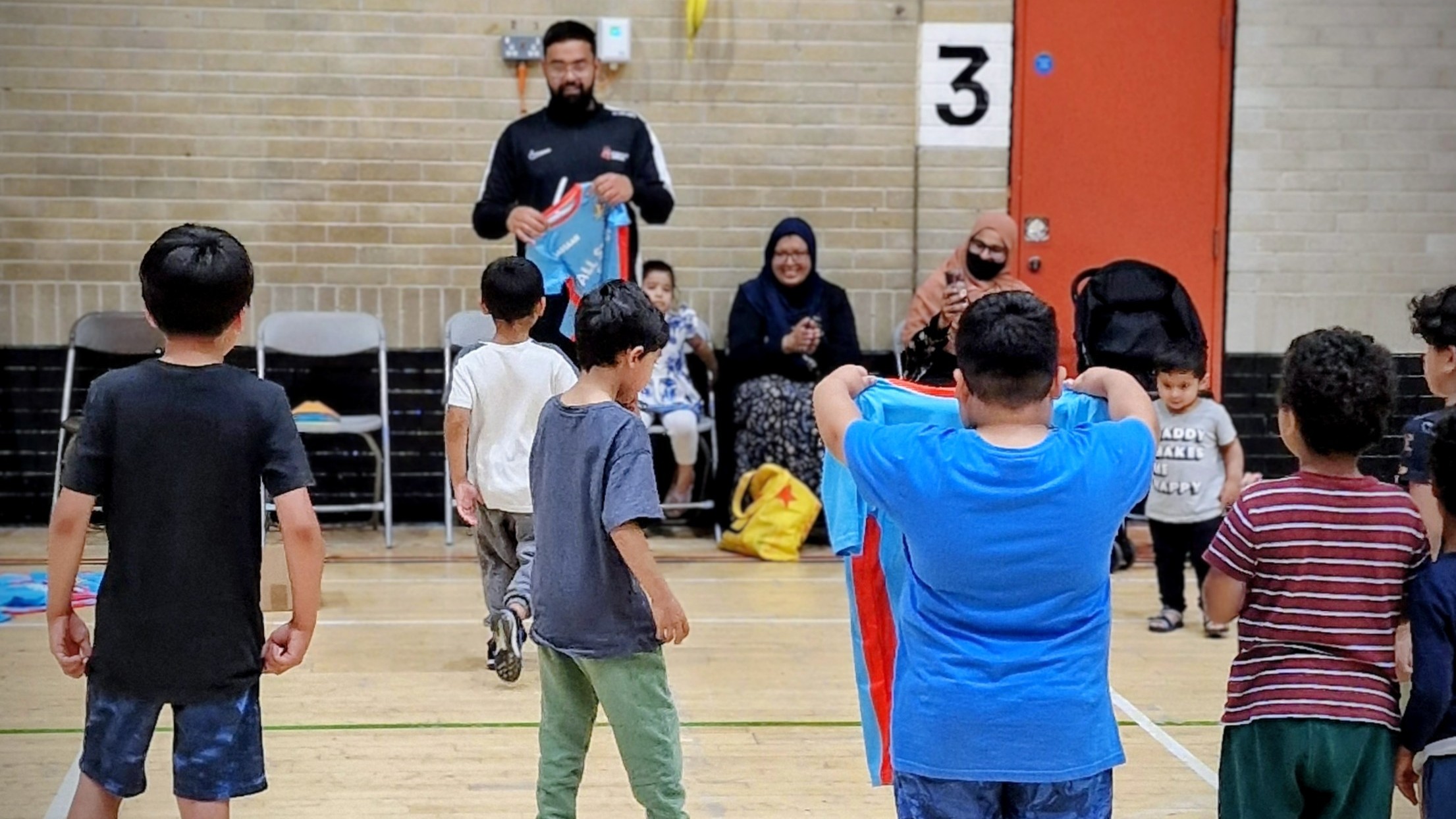 All Stars collect custom shirts from head coach at Concord Sports Centre, Sheffield — proud parents clap and smile.