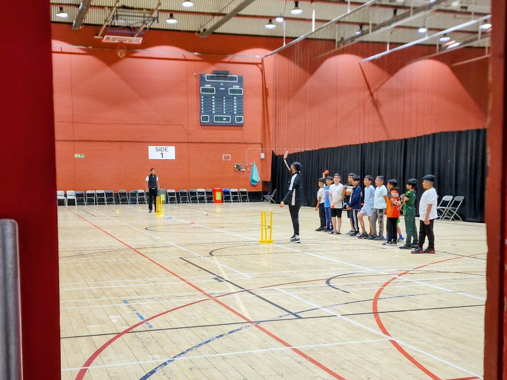 Dynamos players listen to the coach while an assistant sets up at the stumps — indoor session in Sheffield.