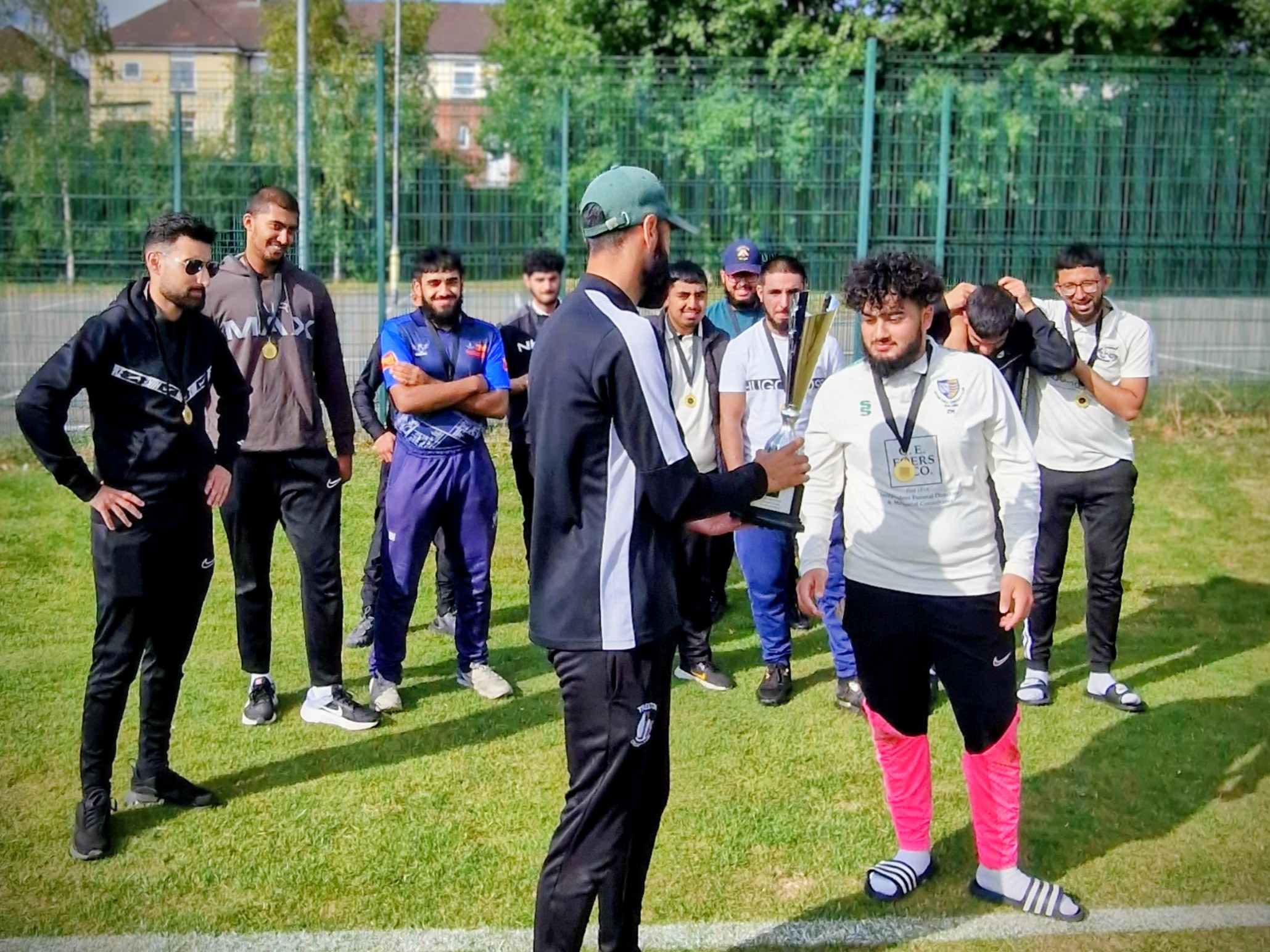 Winning captain Zayn Wasim receives the Youth Hundred 2024 trophy from Cricket Arena presenter as teammates applaud at Shiregreen CC, Sheffield.