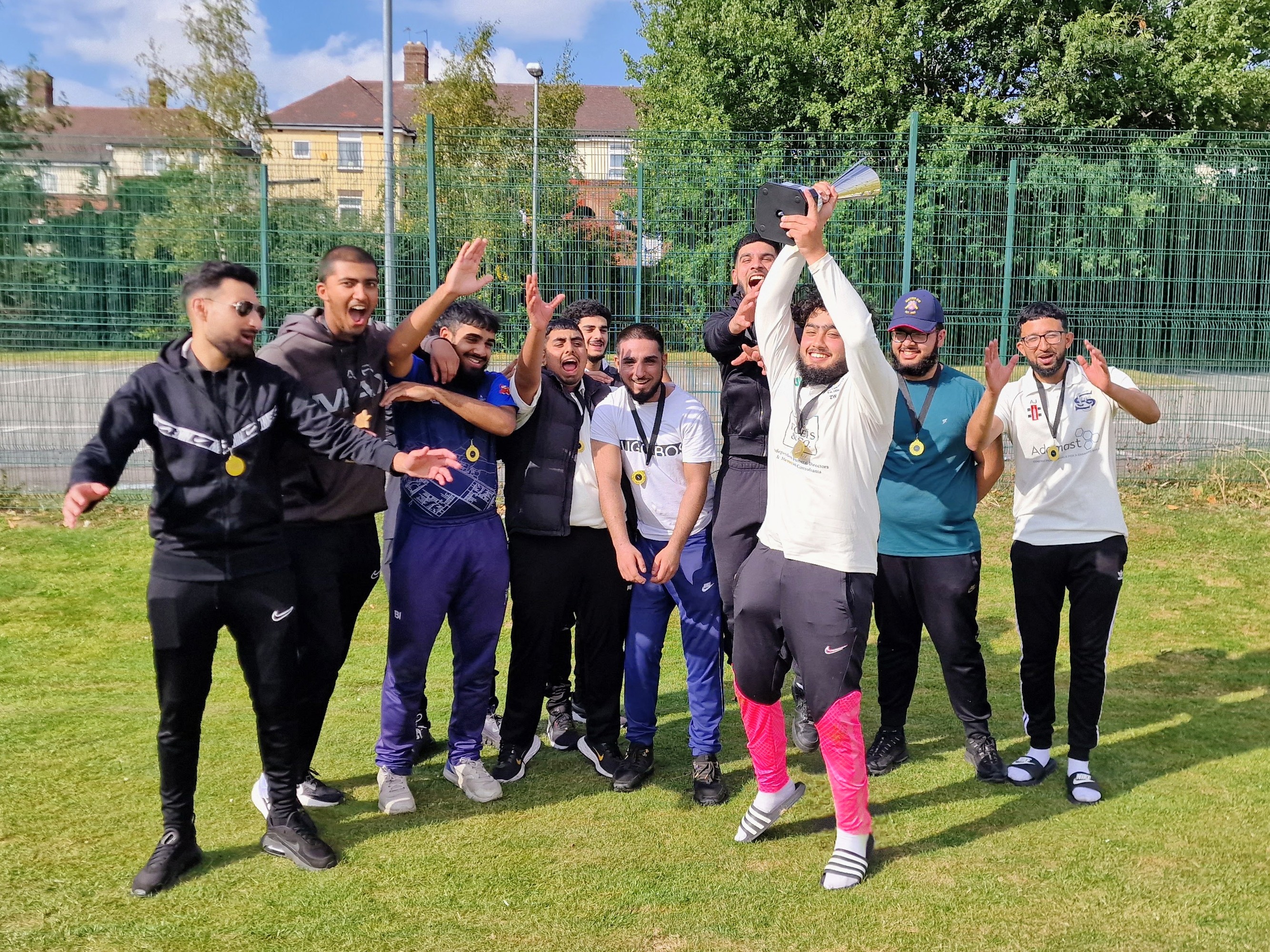 Youth Hundred champions celebrate as captain lifts the trophy high, surrounded by jubilant teammates wearing gold medals in Sheffield.