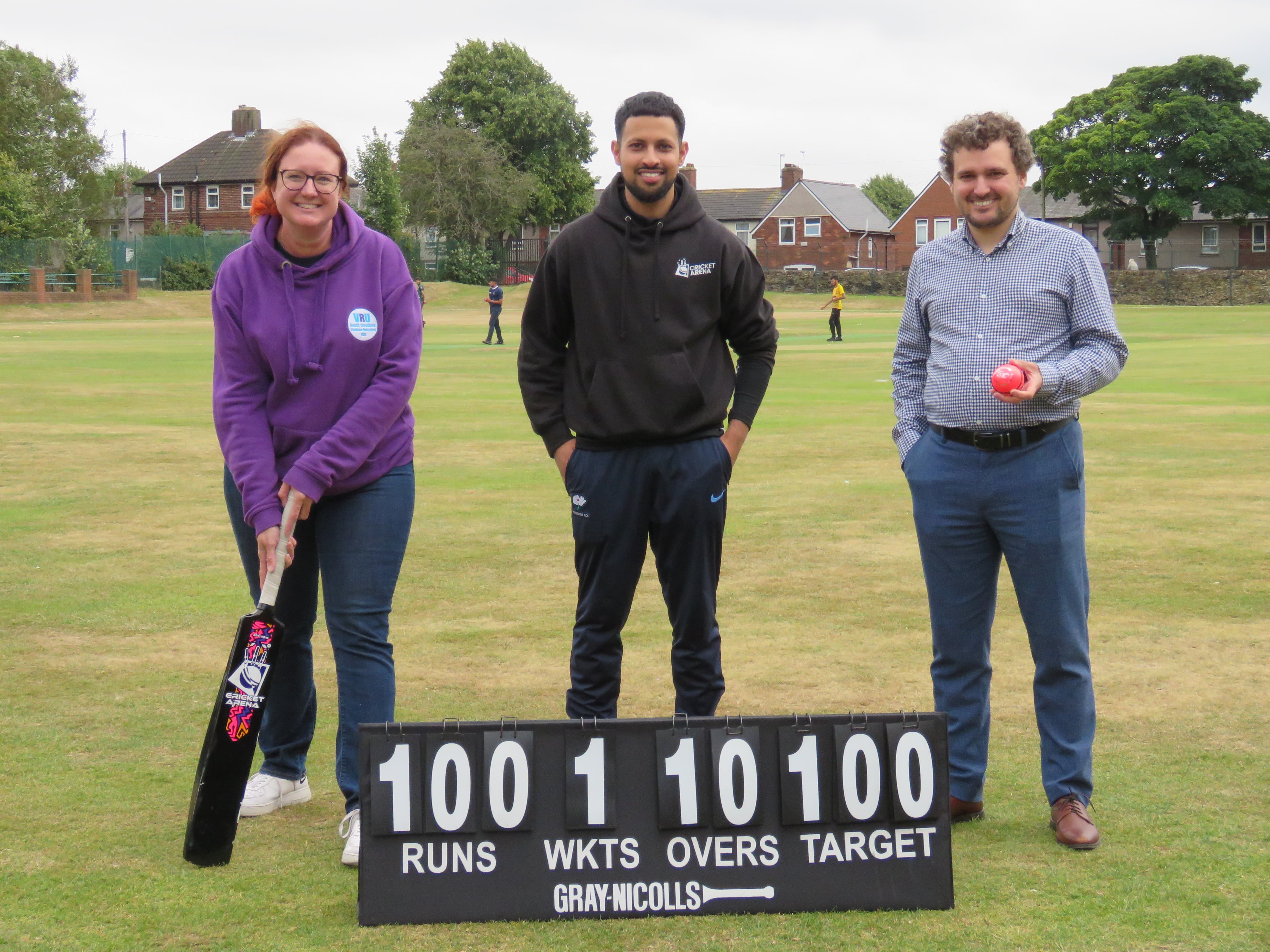Cricket Arena director Hamzah Hussain standing with South Yorkshire Violence Reduction Unit representatives by a scoreboard at Shiregreen Cricket Club.