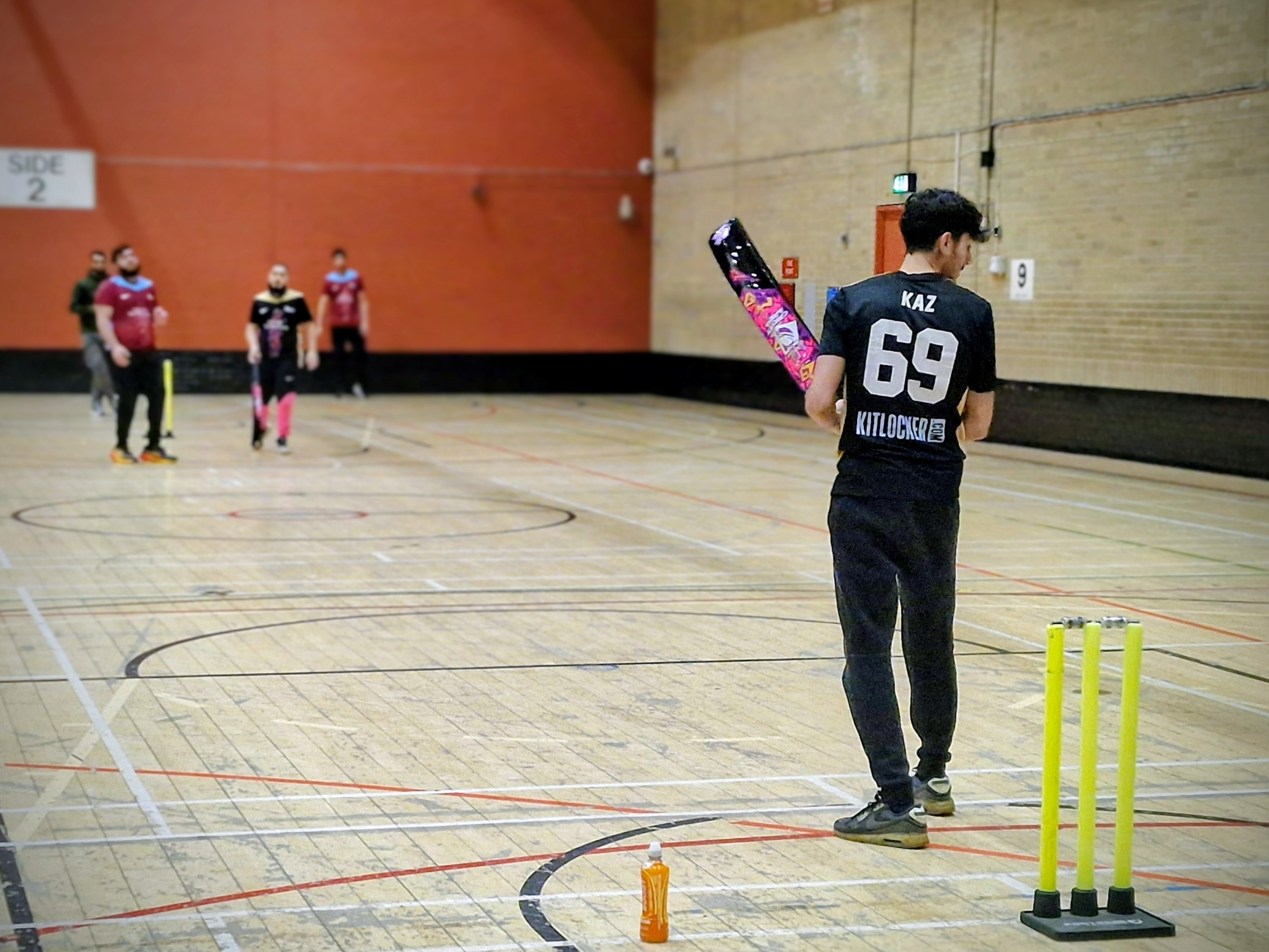 Sharrow Stars player Kaz wearing number 69 black Nike shirt with Kitlocker branding walks to the crease holding a colourful bat during youth indoor cricket at Cricket Arena in Sheffield.