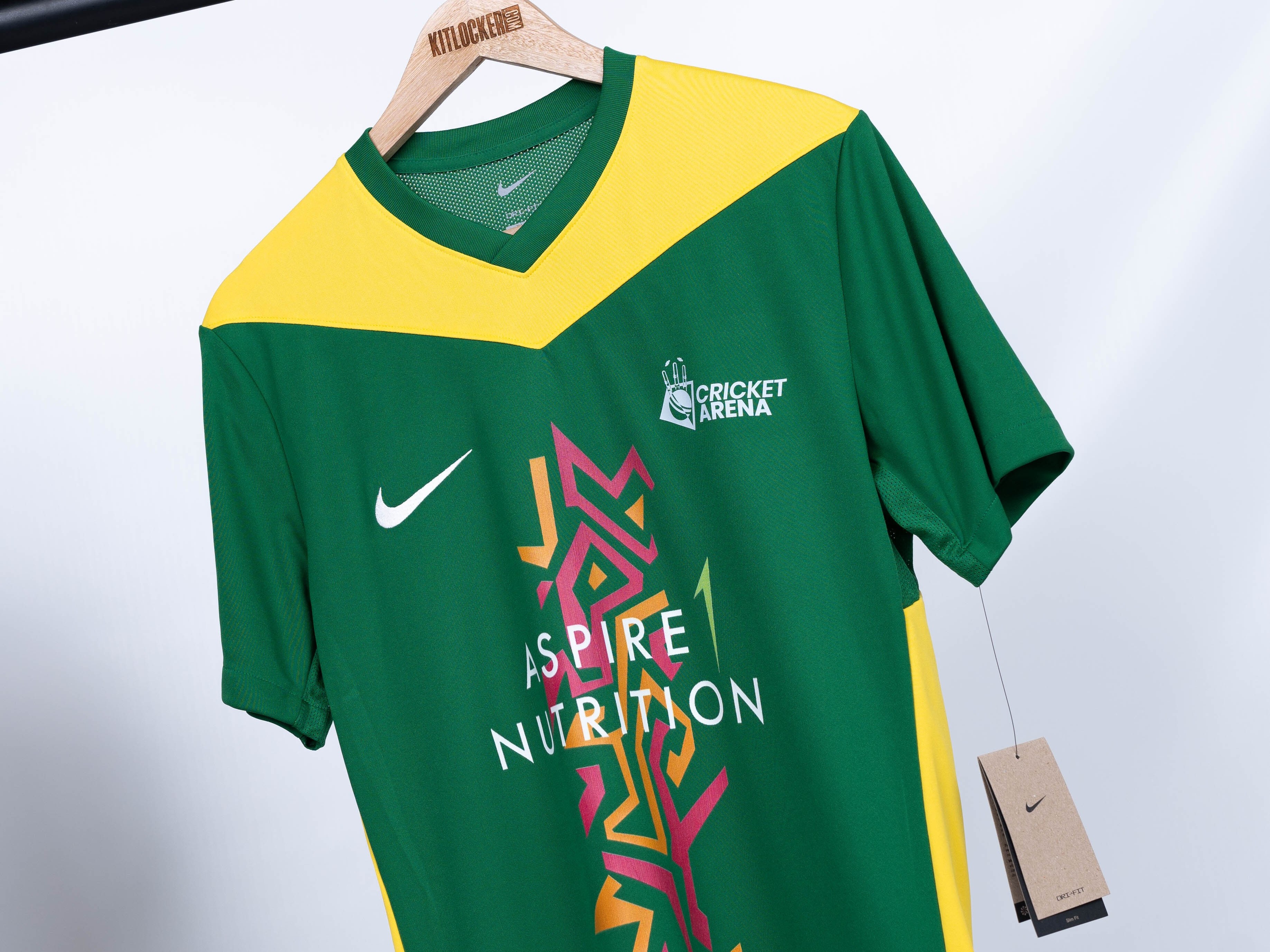 Close-up of green and yellow Shiregreen Nike youth cricket shirt on a Kitlocker hanger showing Cricket Arena and Aspire 1 Nutrition logos.