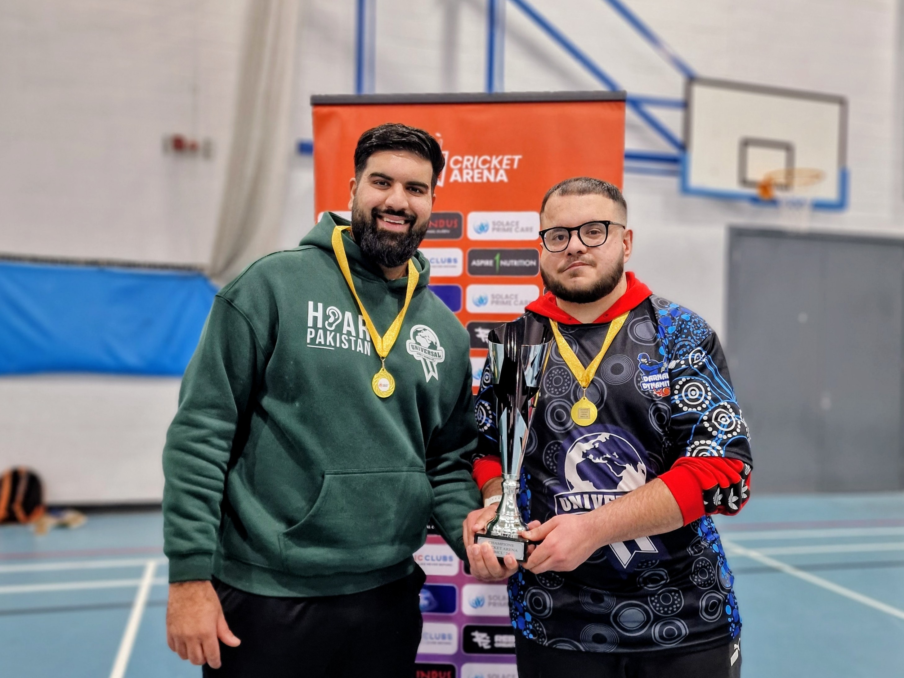 BBICL 2024 winning captain and the Universal Pizza & Burger Bar sponsor representative hold the champions trophy together, showing the impact of kit sponsors.