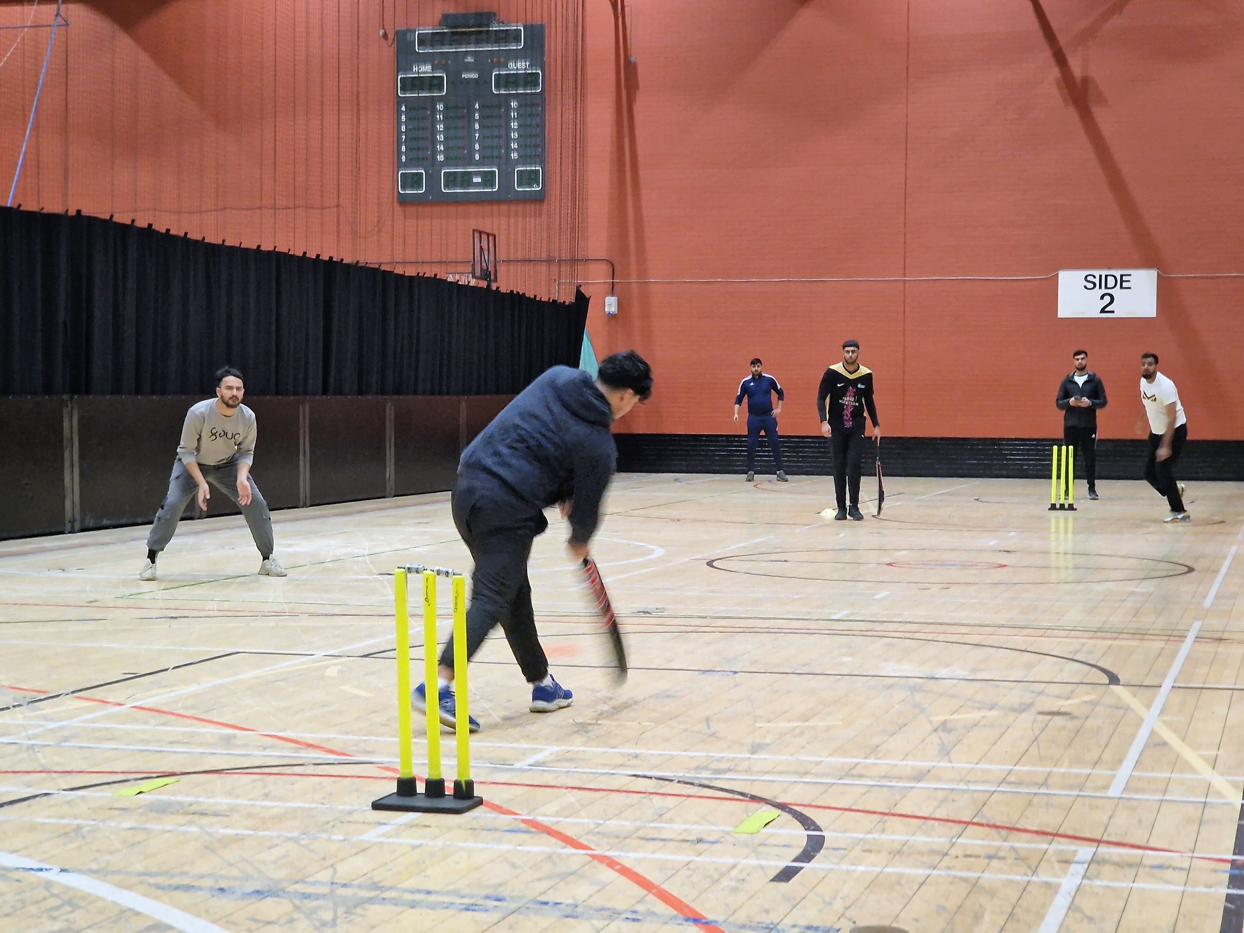 Batter plays a shot with fielders set during a Sheffield Cup 2025 indoor cricket game at Concord Sports Centre in Sheffield.