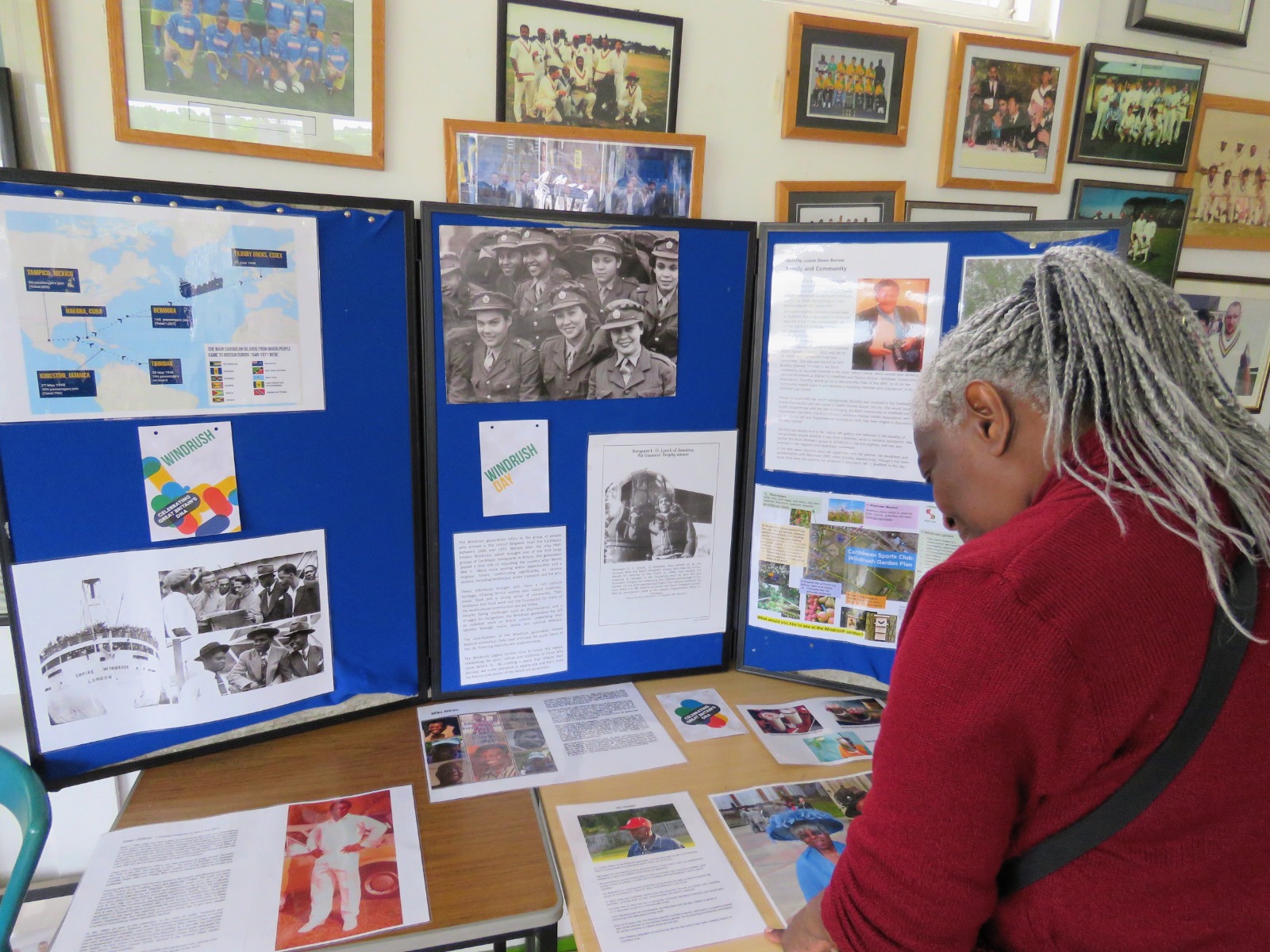 Visitor reading Windrush history displays on blue boards inside the Caribbean Sports Club pavilion.