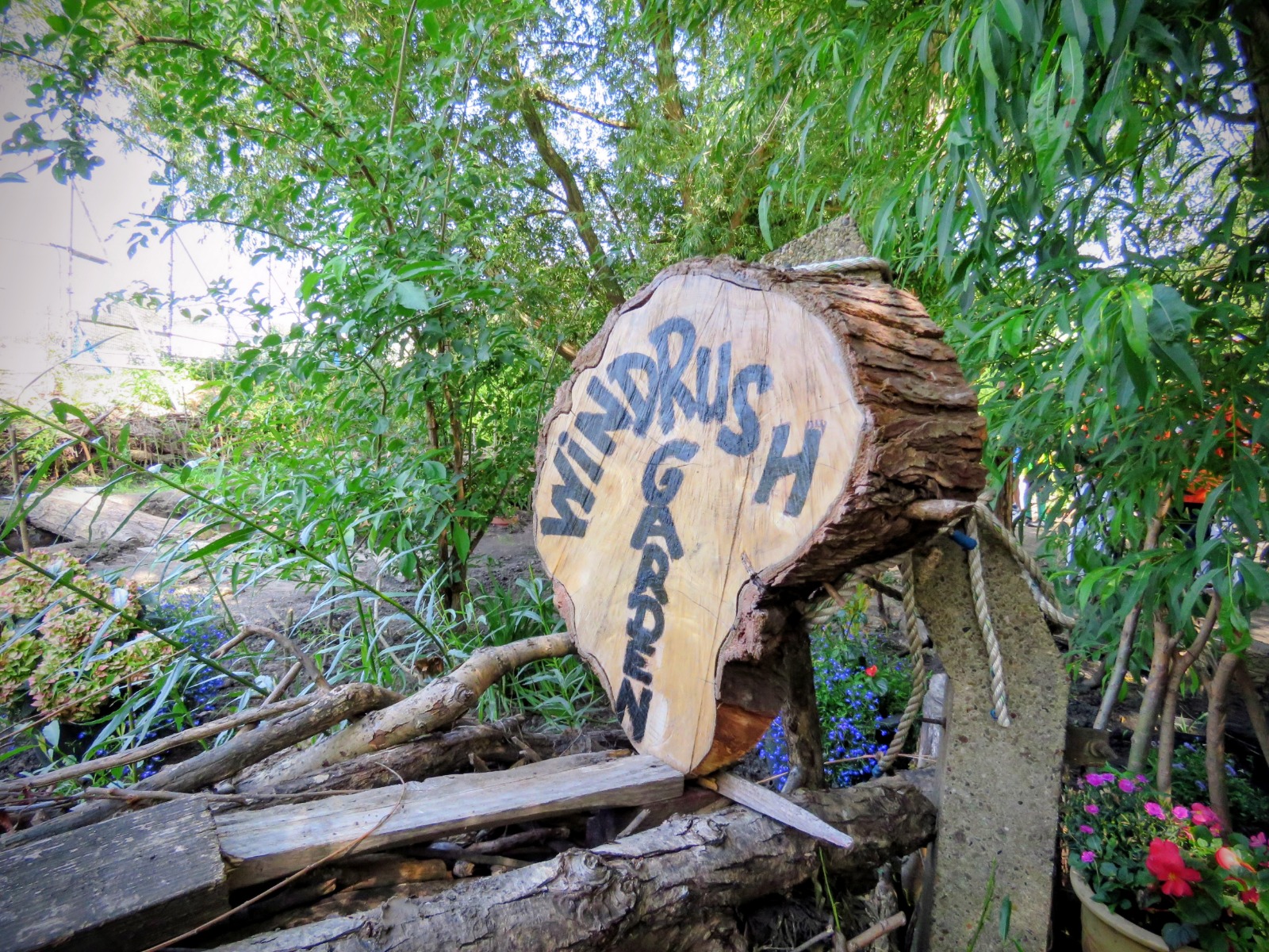 Wooden Windrush Garden sign surrounded by green plants at Caribbean Sports Club in Sheffield.
