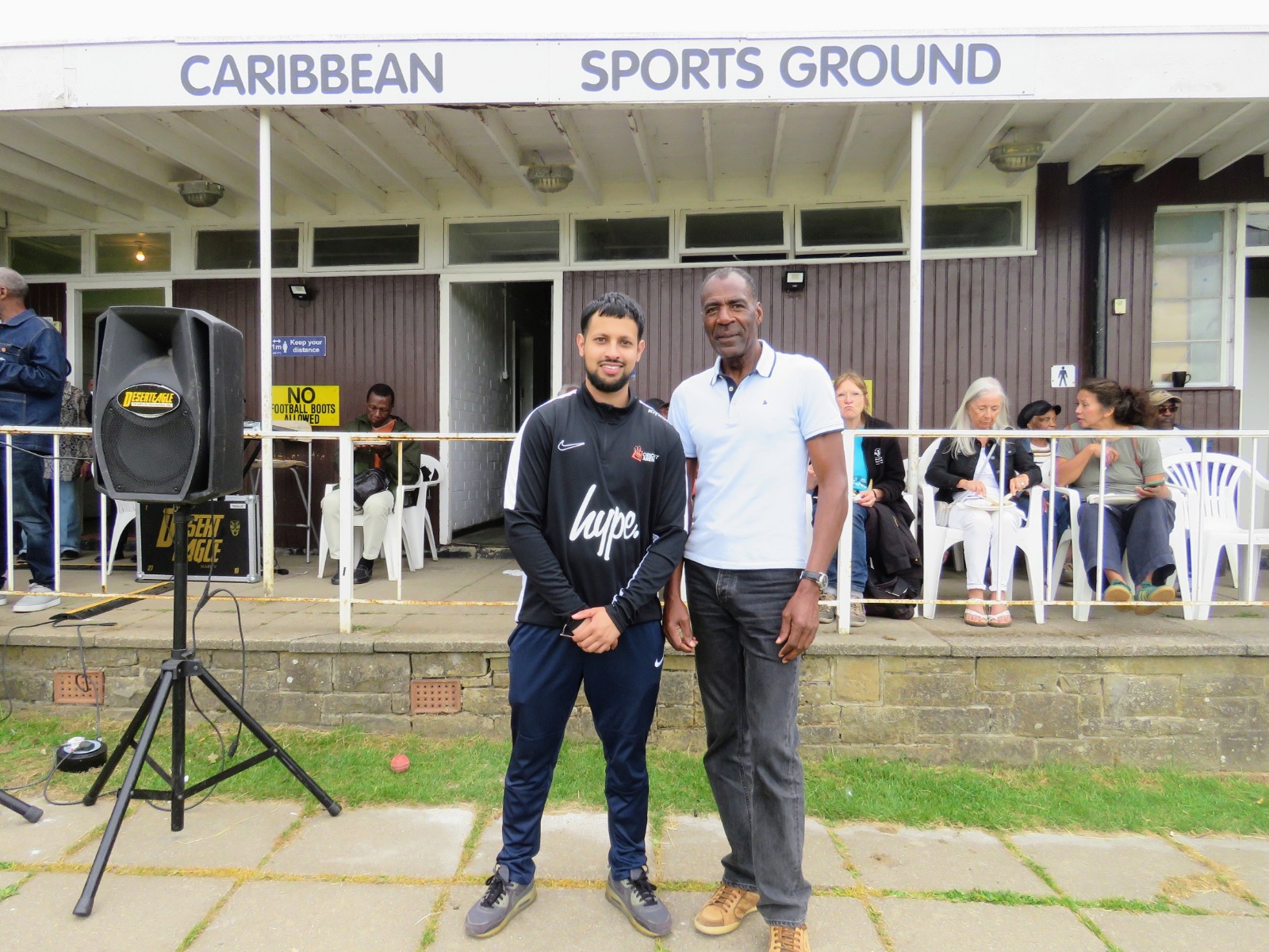 Cricket Arena director standing with the Caribbean Sports Club chairman outside the pavilion on Windrush Day.