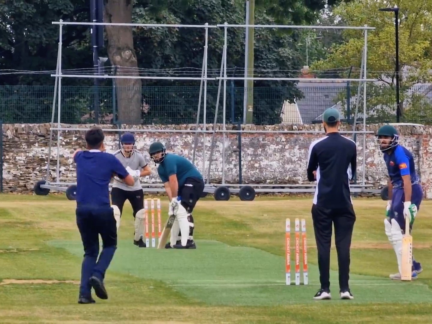 A bowler charges in during a youth hundred match at Shiregreen in Sheffield, with batters and umpire focused on the next ball.
