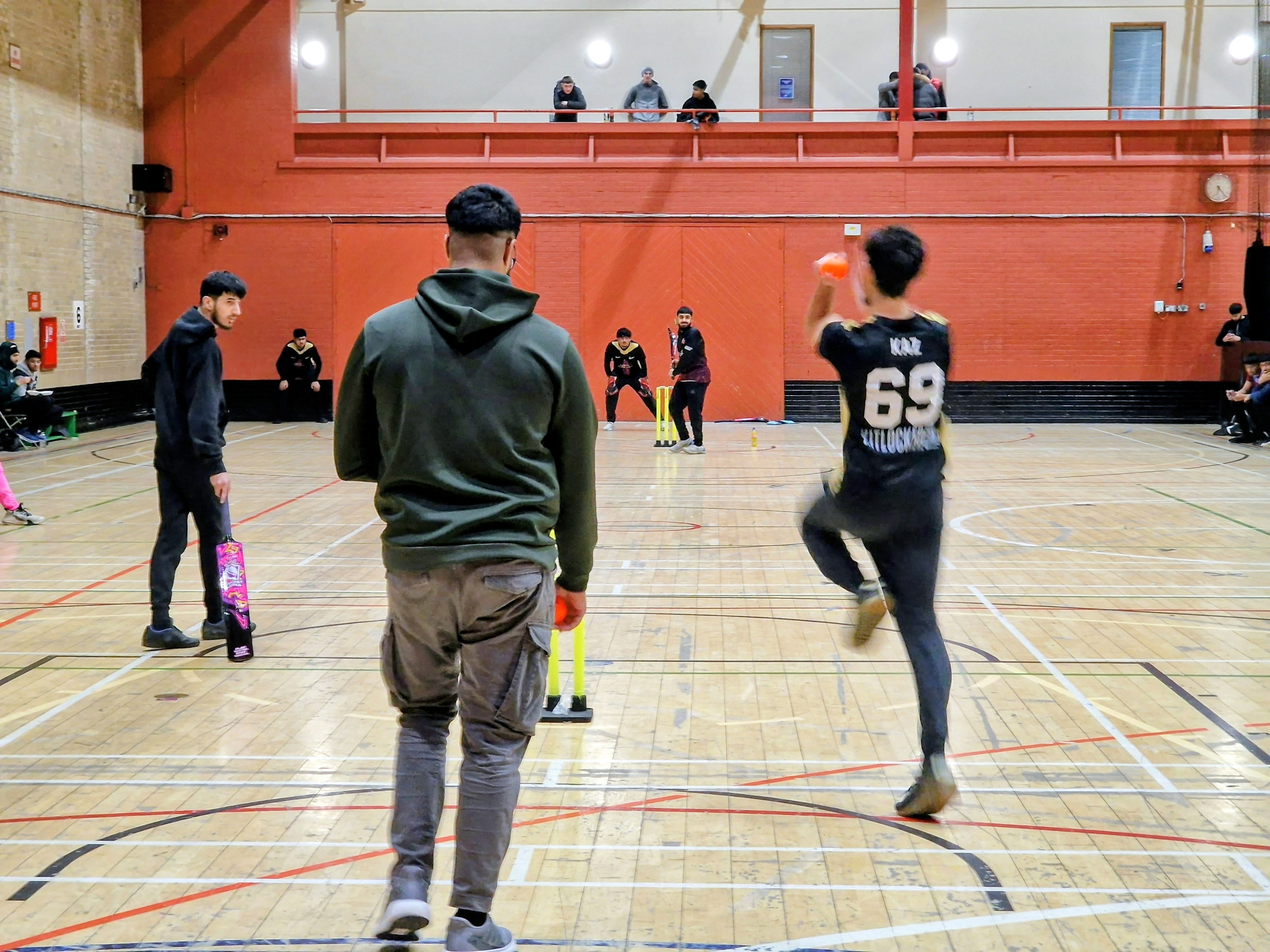 Young players compete in an MBL indoor cricket match in Sheffield, with a bowler running in and batters ready at the crease.