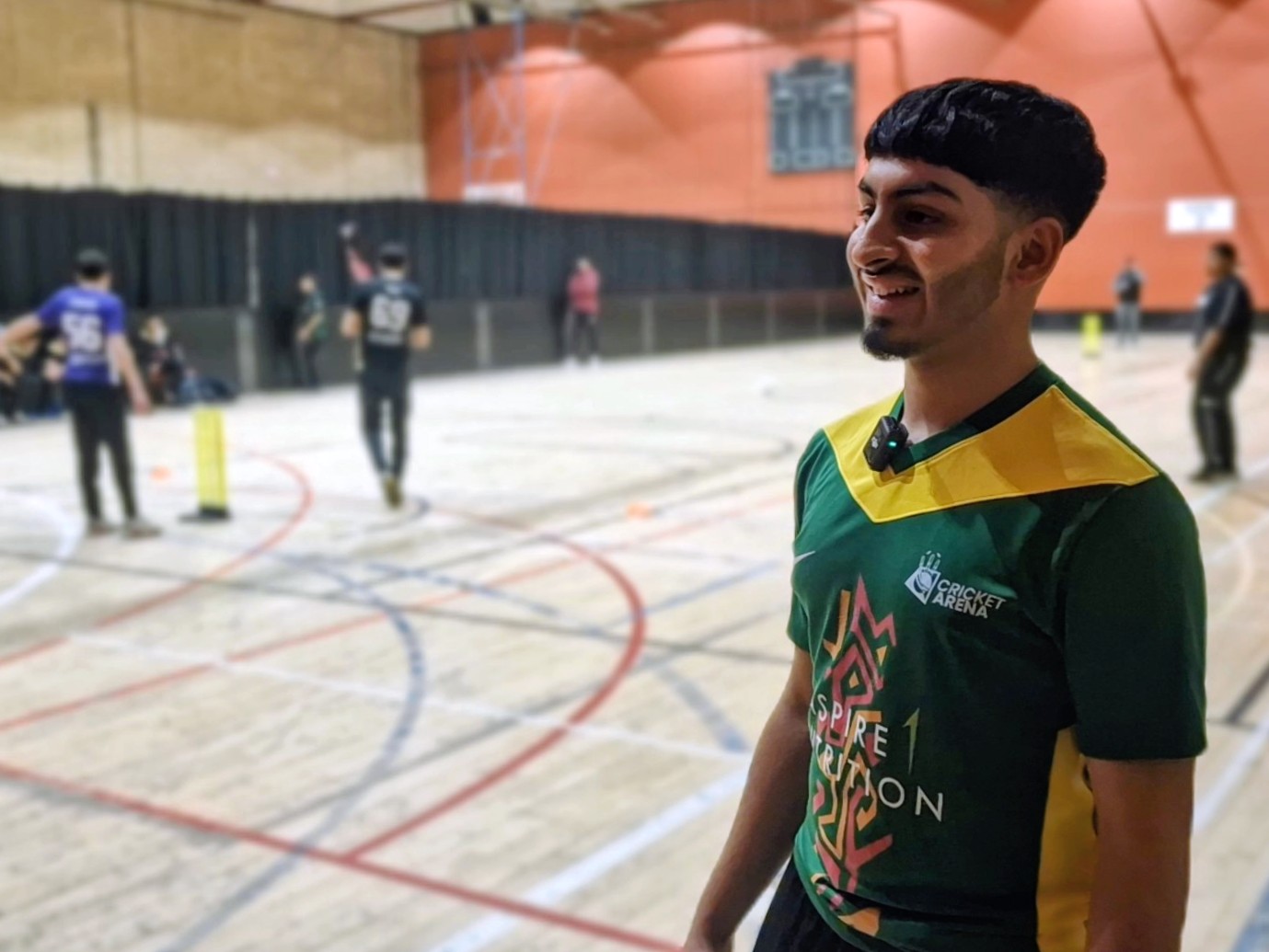 A young player smiles courtside during an MBL indoor cricket game in Sheffield, wearing a mic as he shares his experience of the programme.