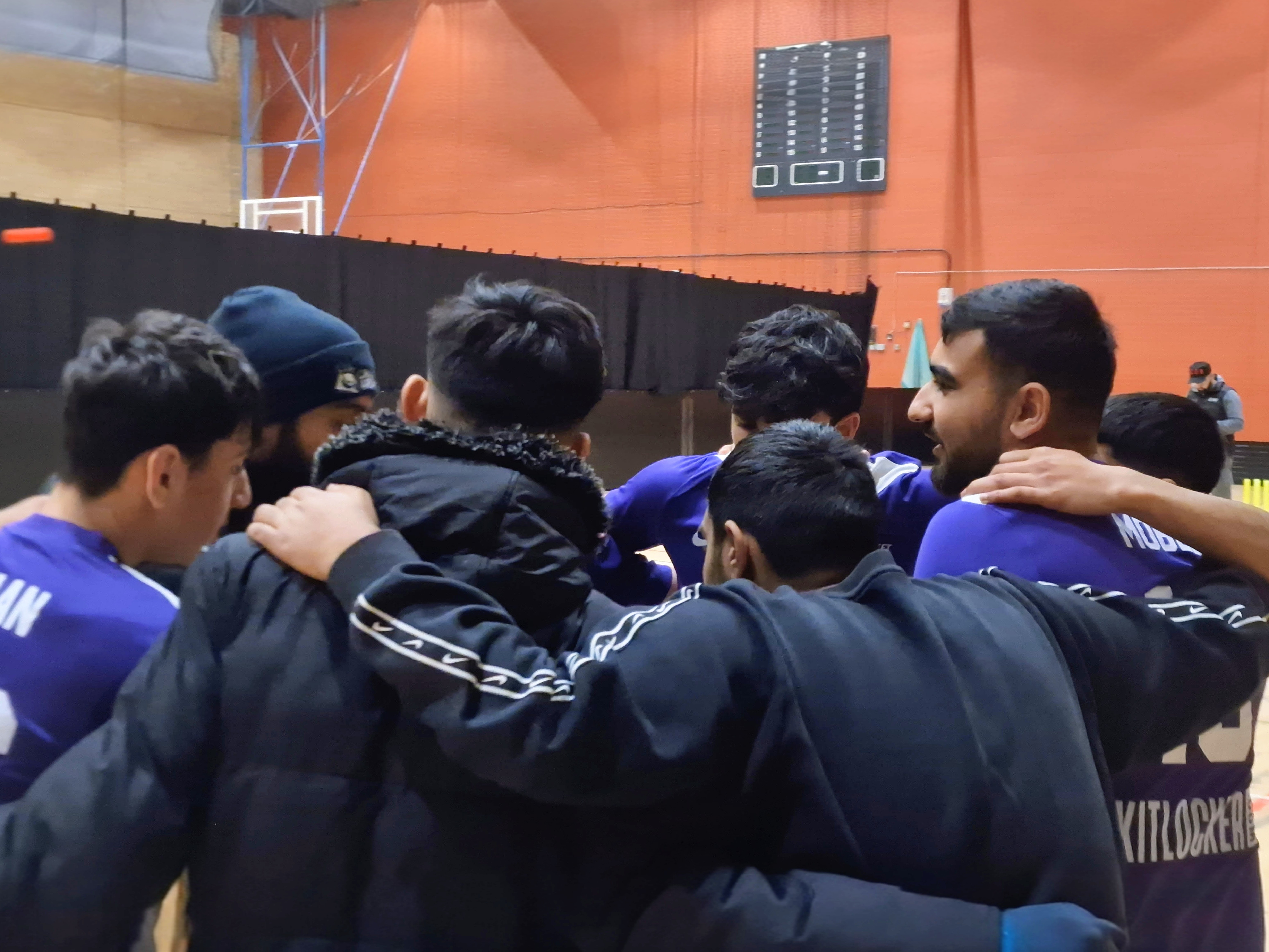 n indoor cricket team huddle with arms around each other, sharing tactics and encouragement before their MBL game in Sheffield.
