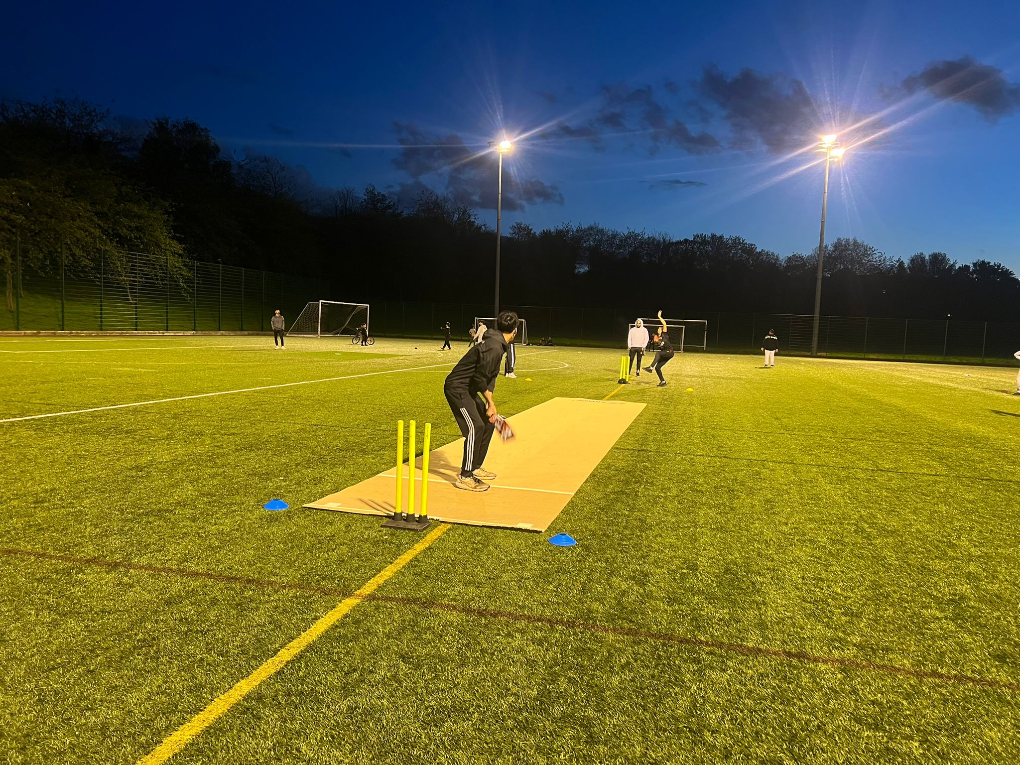 Young people play cricket under the floodlights at Fir Vale School in Sheffield, using a Flicx pitch for a safe evening community session.