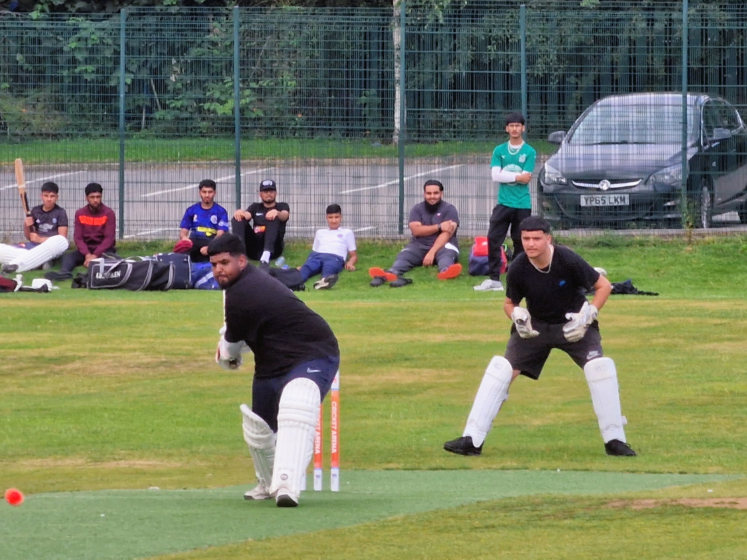 A young batter plays a shot in the youth hundred hardball competition at Shiregreen Cricket Club while his keeper and teammates watch on.