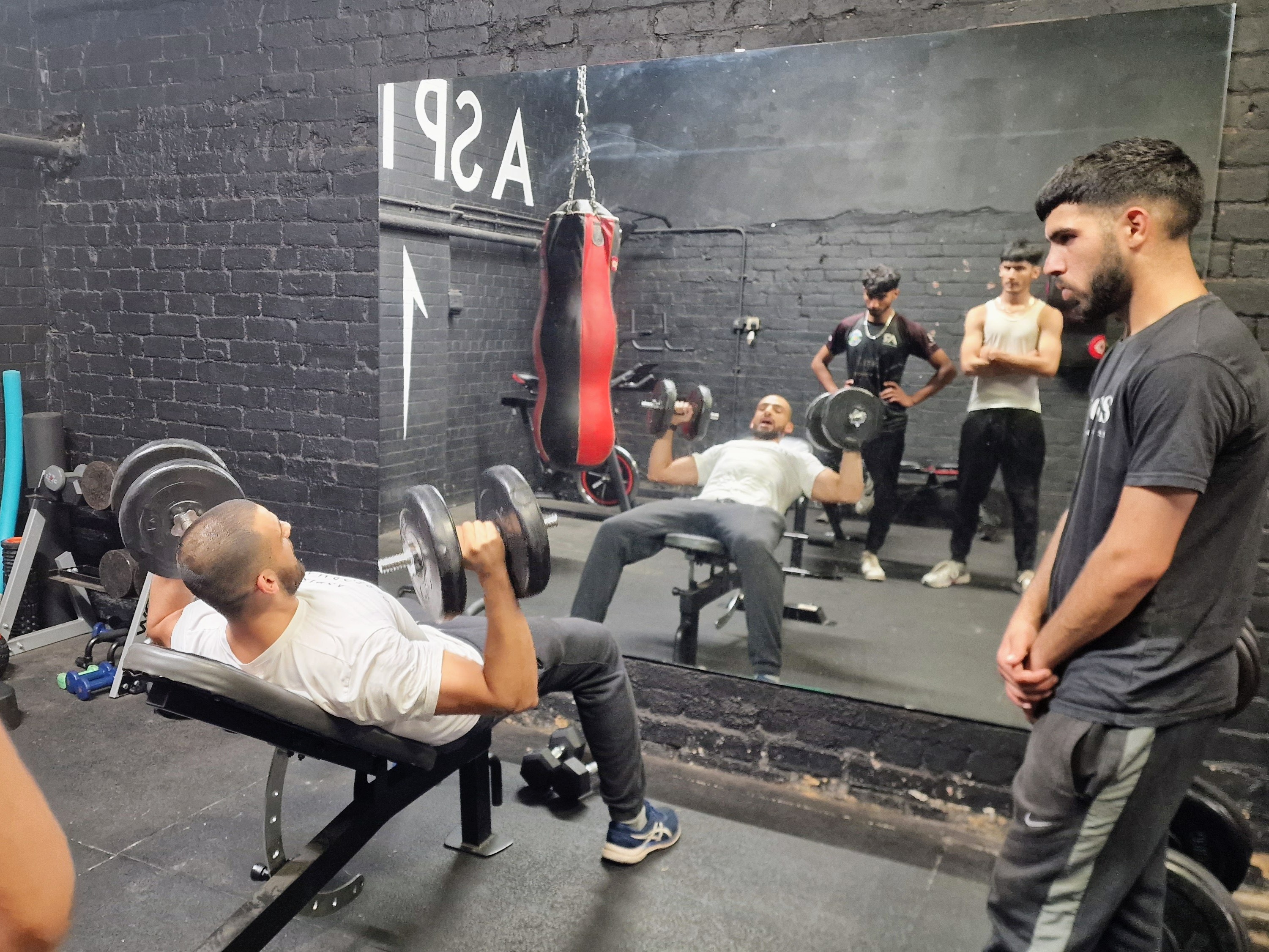 Mazin demonstrates safe dumbbell technique at Aspire 1 Performance gym in Sheffield while young men watch and learn in a Cricket Arena workshop.