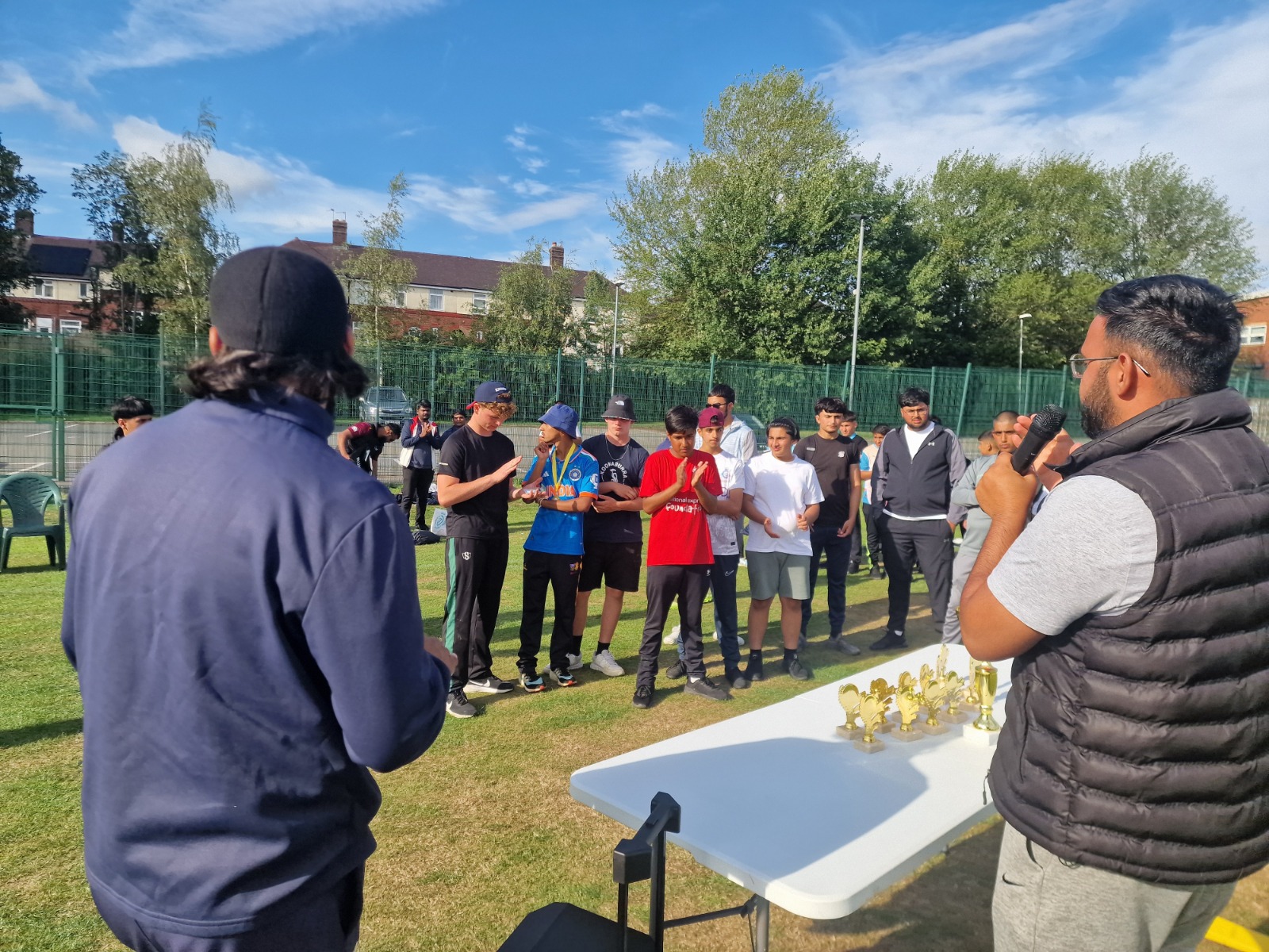 Cricket Arena organiser speaks into a microphone during the Junior Hundred 2025 awards ceremony as players line up with trophies in Sheffield.
