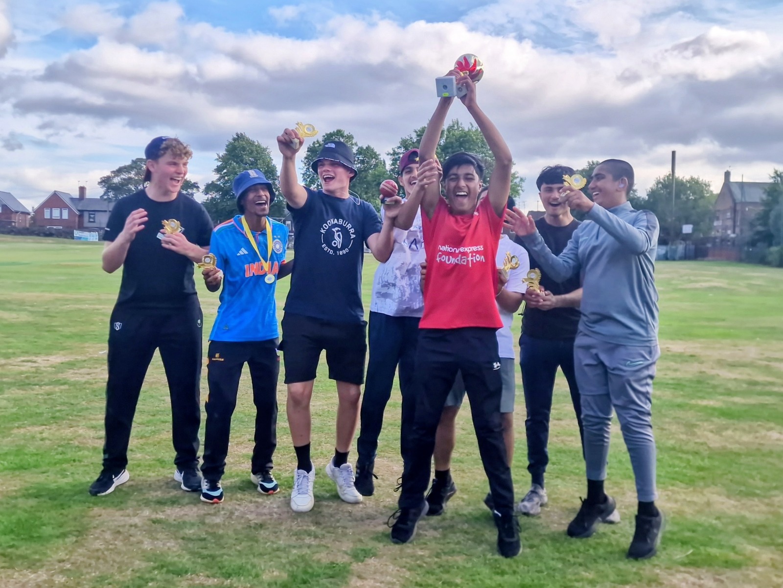 Sharrow Stars junior team jump and cheer on the outfield, raising the Junior Hundred 2025 winners’ trophy at Shiregreen Cricket Club in Sheffield.