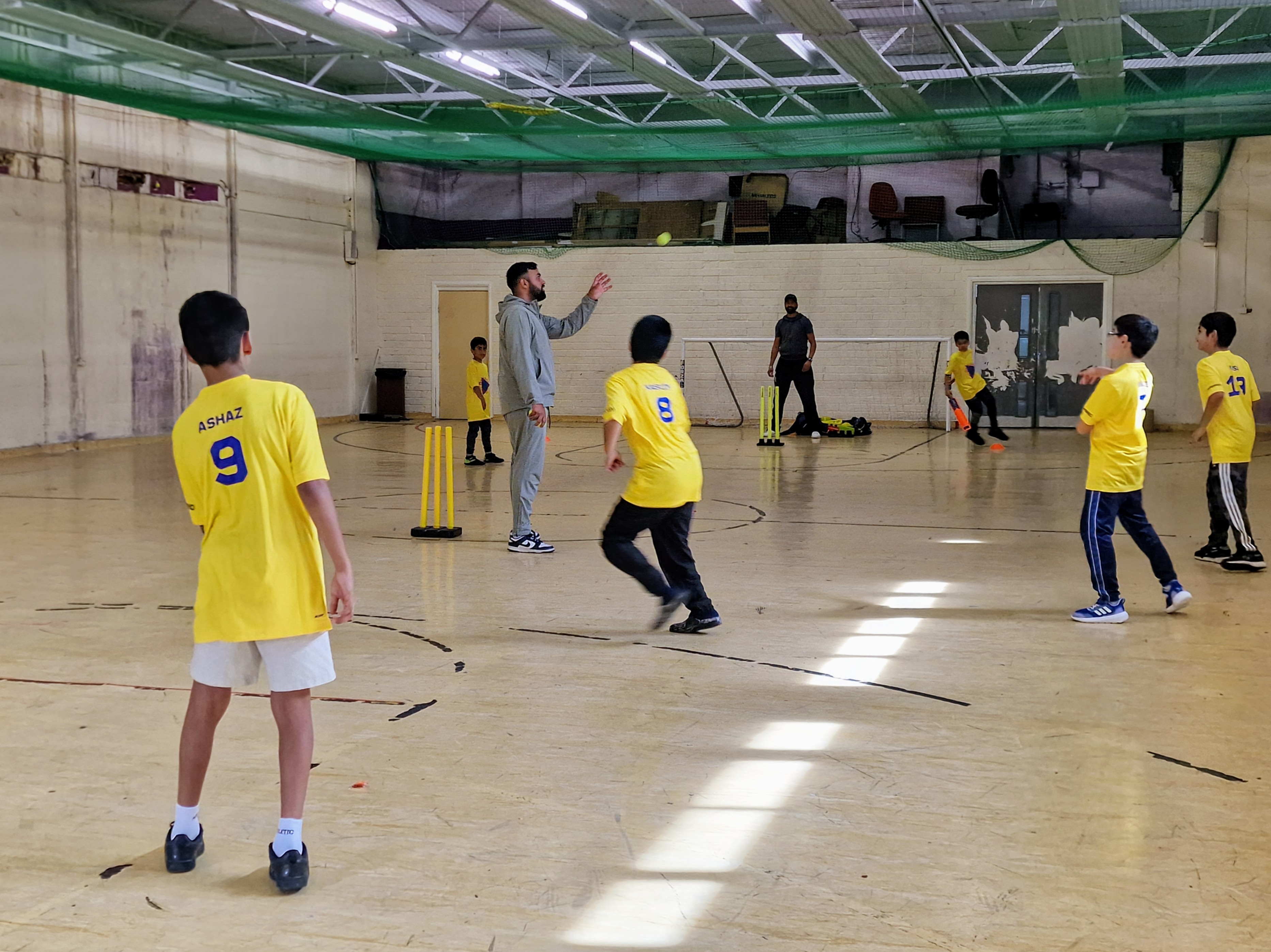 Dynamos players practise catching and fielding while a coach tosses the ball in the YMA sports hall.