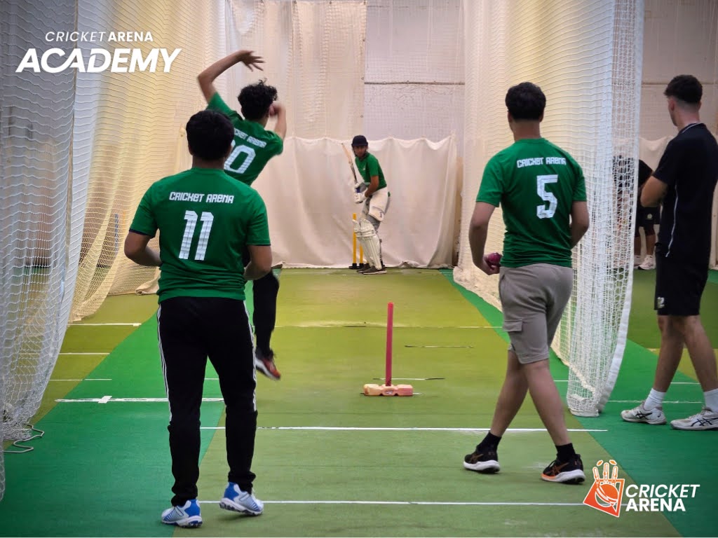 A bowler runs in as a batter takes guard in the indoor nets at Cricket Arena Academy, Sheffield, where hardball training builds match-ready technique.