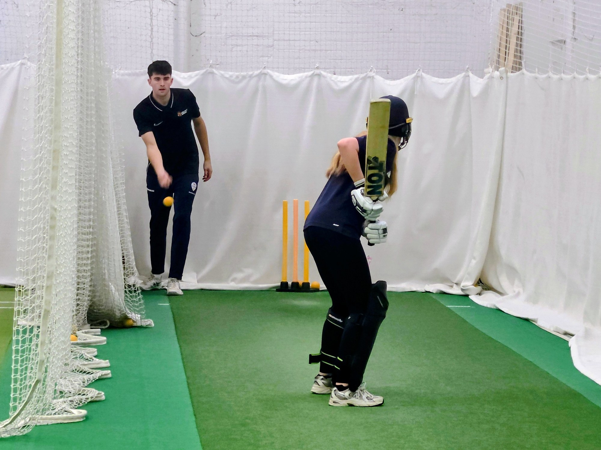 A coach feeds throwdowns to a Girls Academy batter in Sheffield, close technical work that sharpens shot selection.