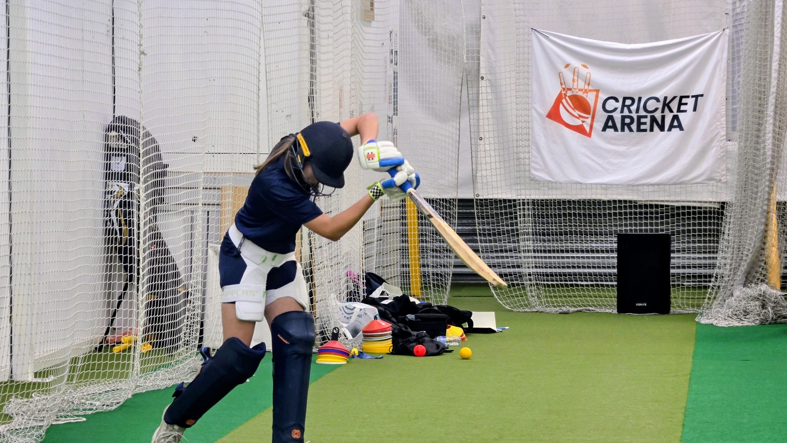 A girl drives through the line in the indoor nets at Cricket Arena Academy in Sheffield, hardball batting for girls aged 13-16.