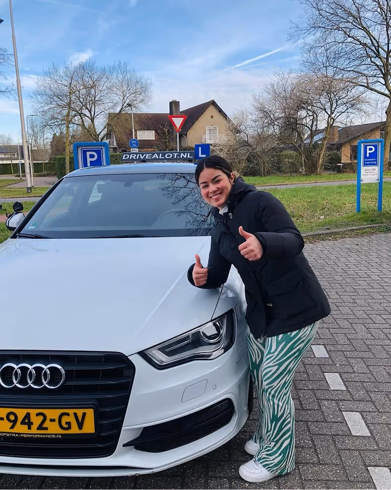 Happy female driving student with white Audi at Drivealot.nl, smiling and giving thumbs up