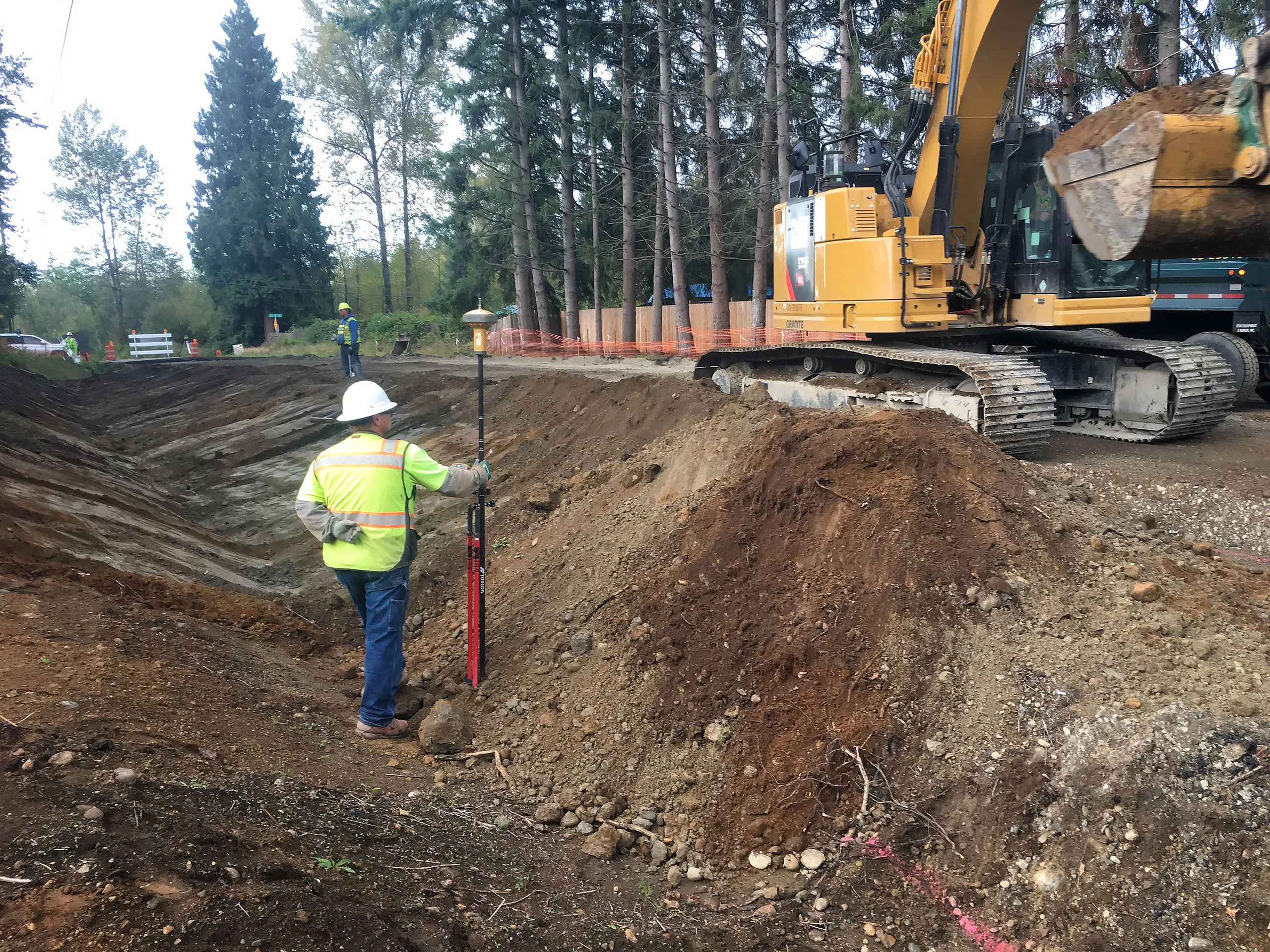 A man in a yellow vest stands next to a large pile of dirt.