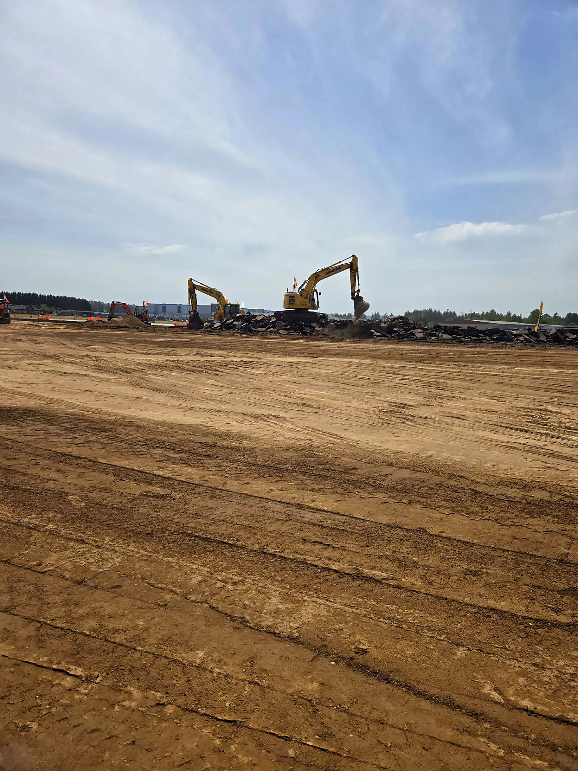 A dirt field with a yellow tractor and a yellow backhoe.
