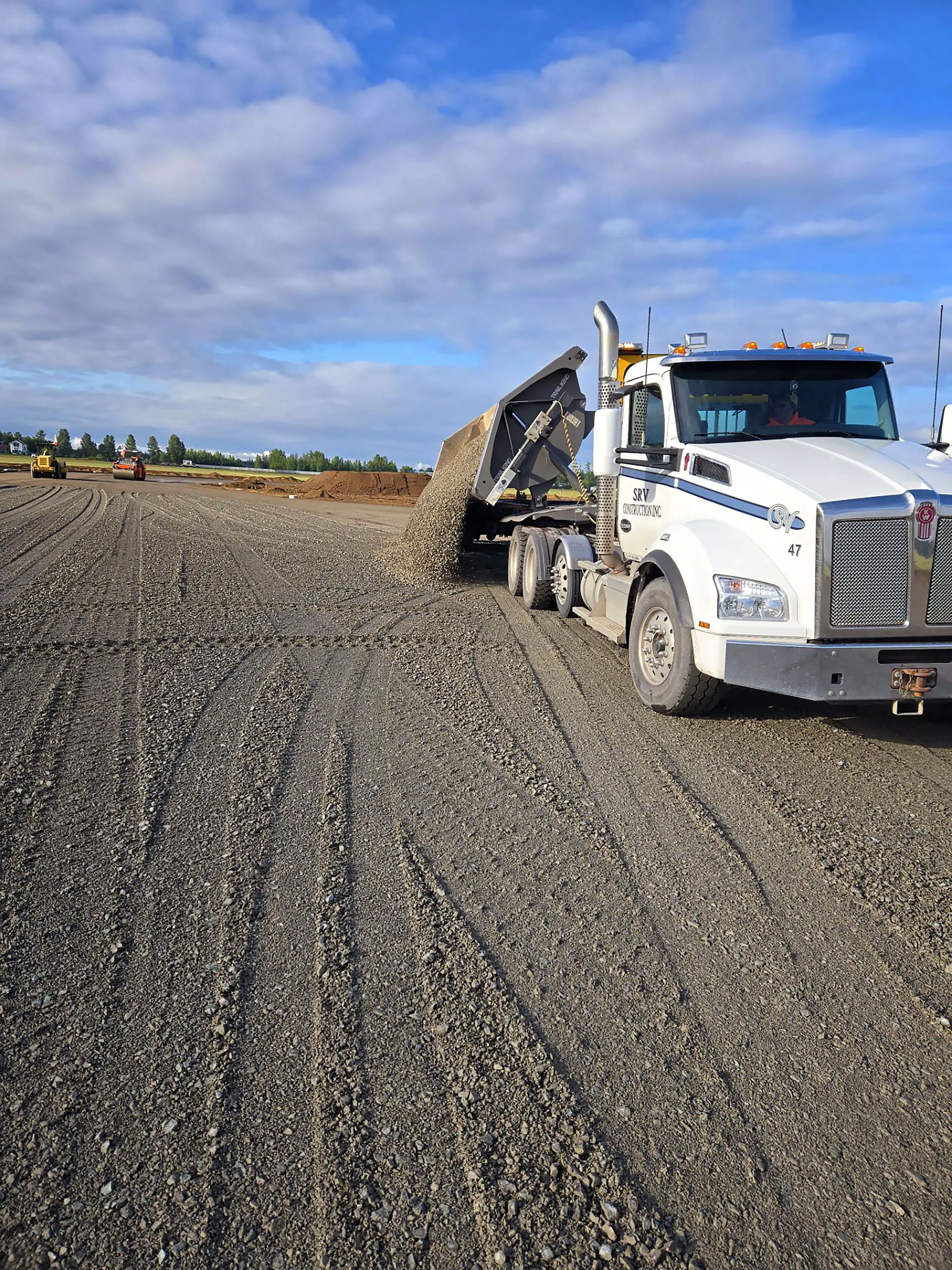 A dump truck is parked on a gravel road.
