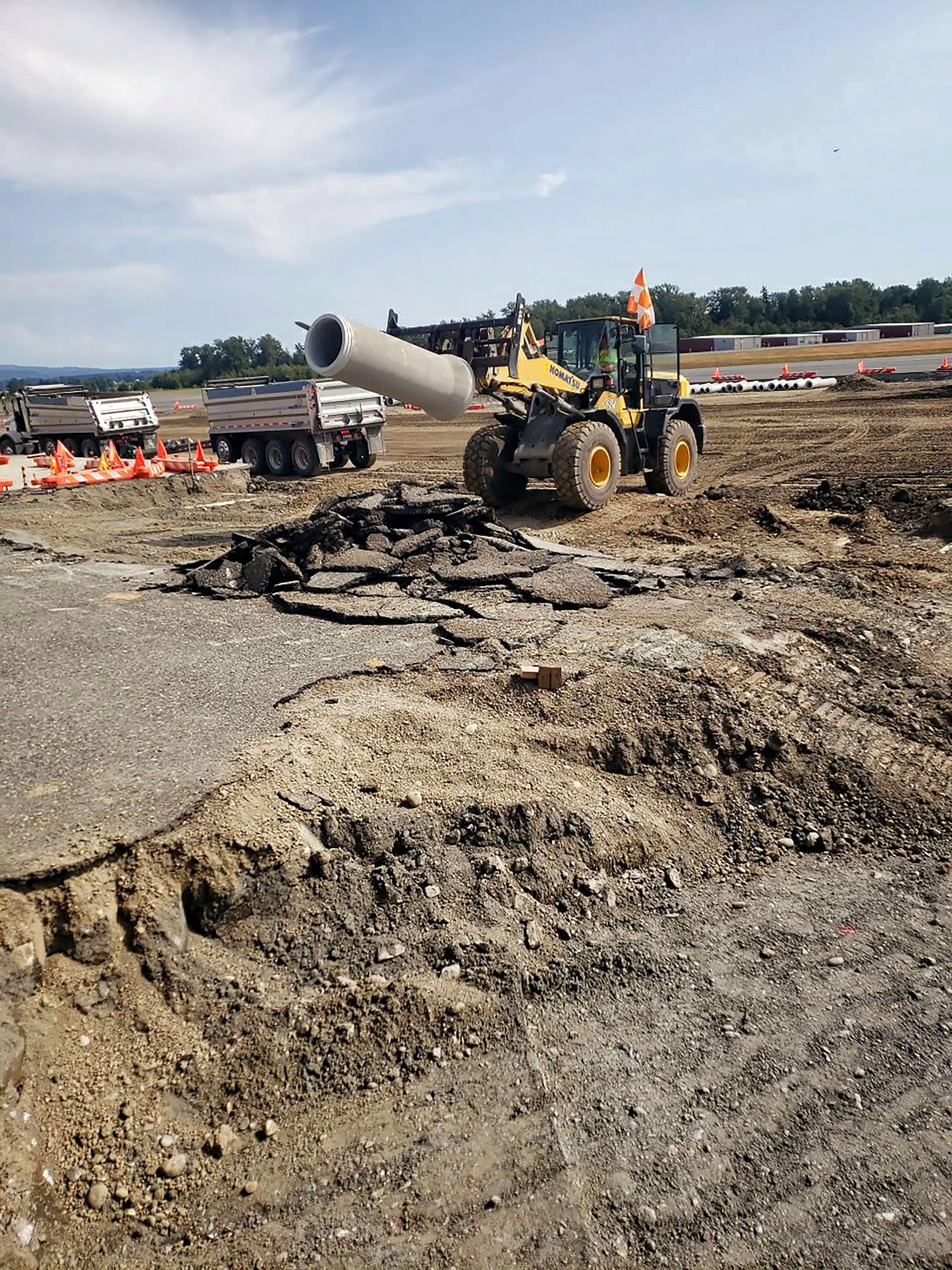 A yellow bulldozer is moving a large pipe.