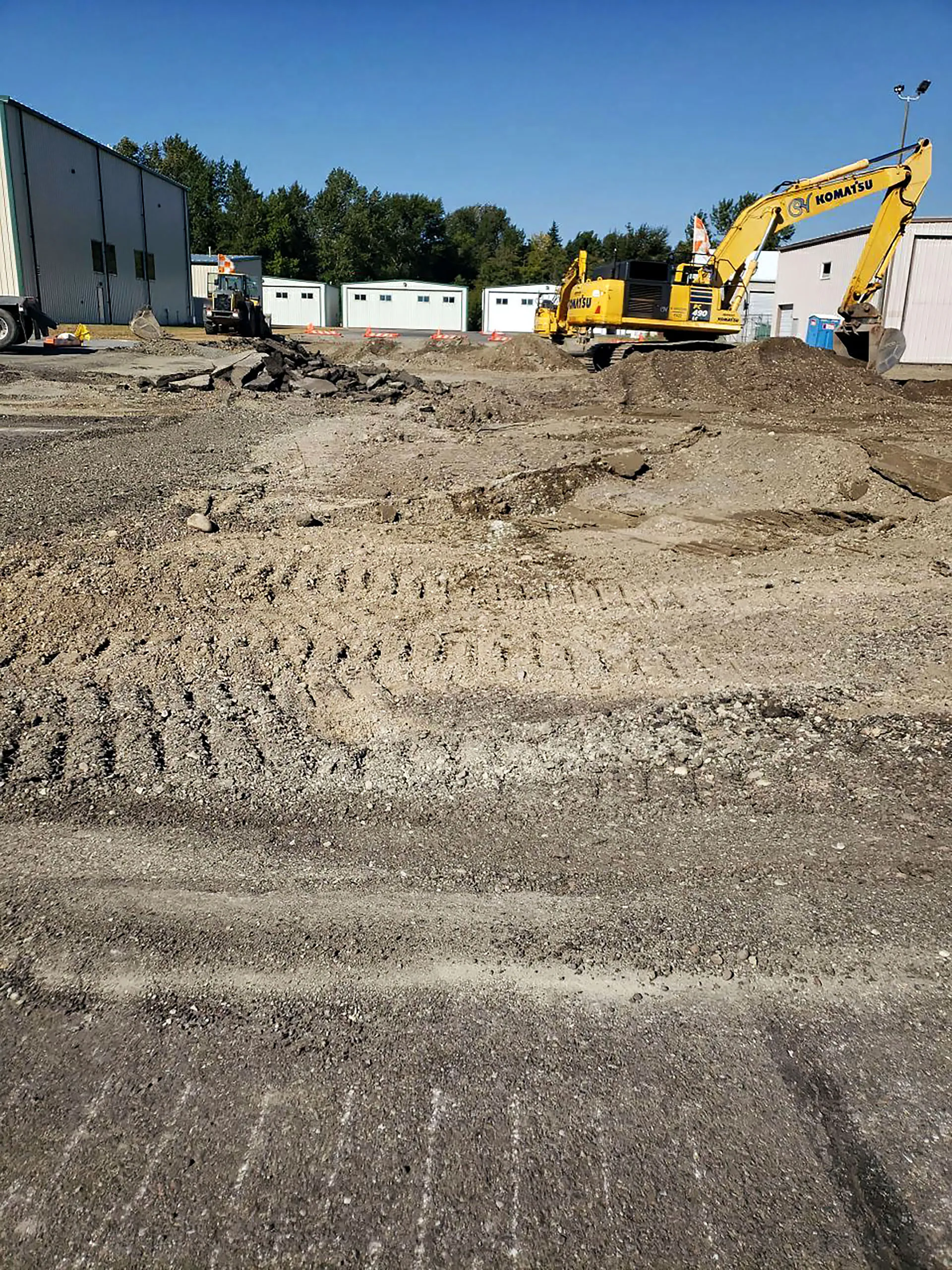 A large dirt field with a yellow bulldozer in it.