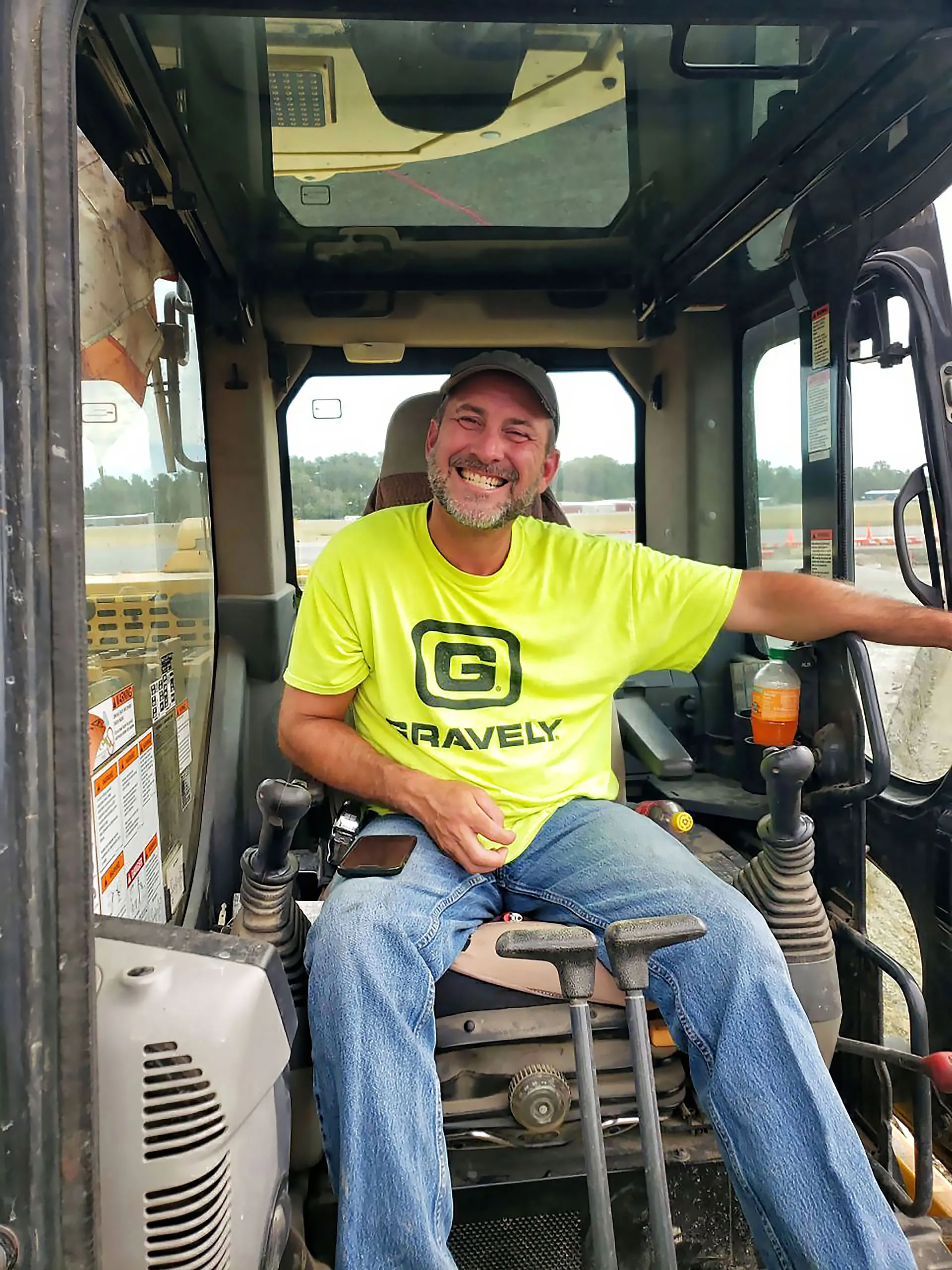 A man wearing a yellow shirt and a hat is sitting in a bulldozer.