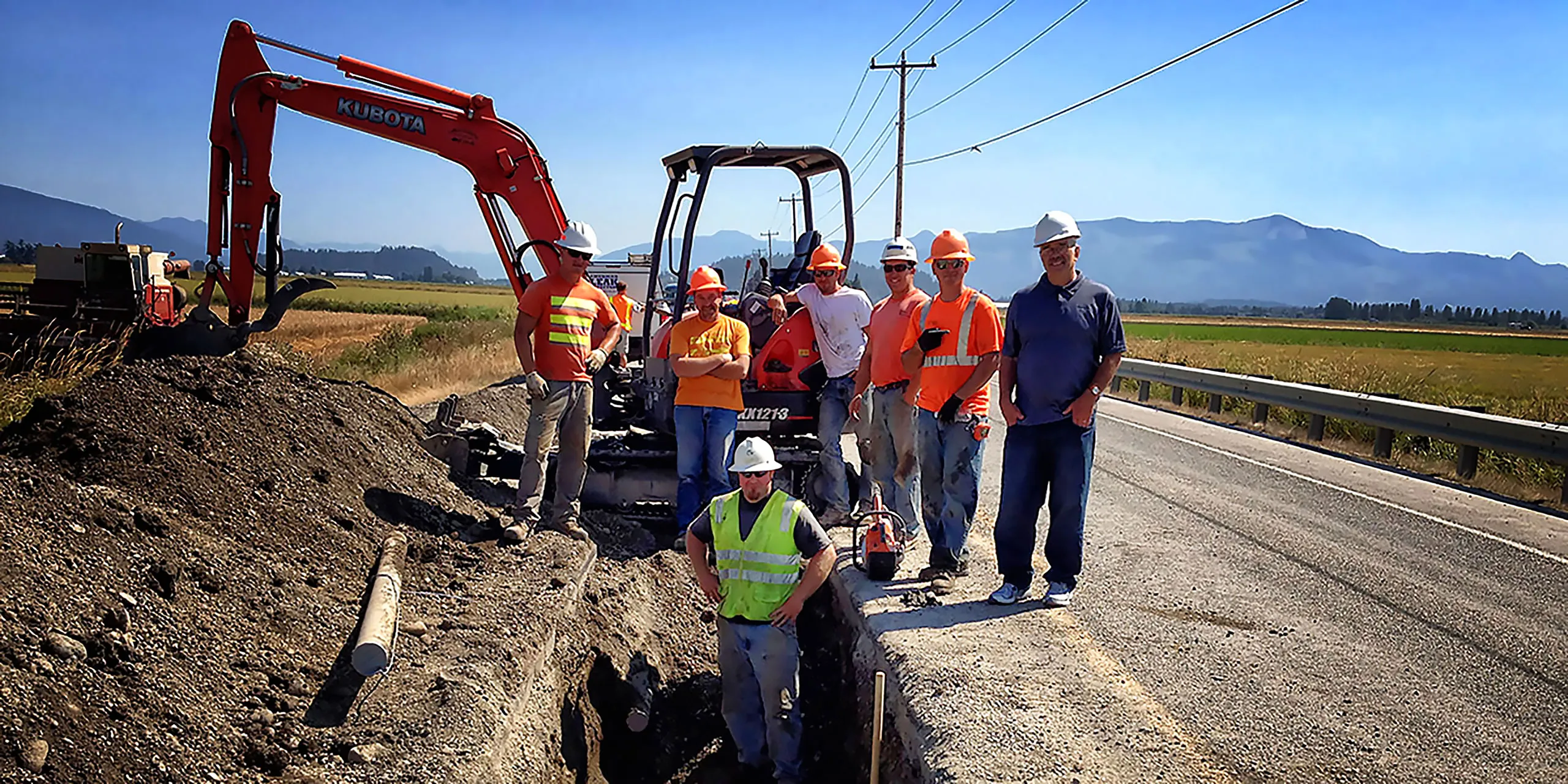 A group of construction workers standing in front of a large excavator.