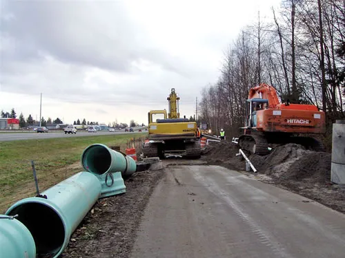 A road with a yellow construction vehicle and a large pipe.